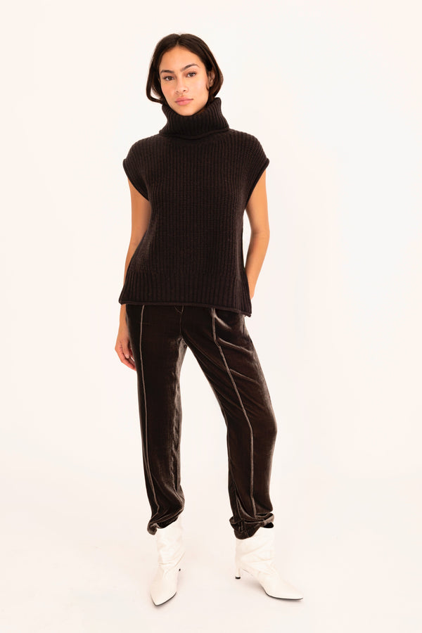 Person wearing a brown sleeveless turtleneck and pants on a white background