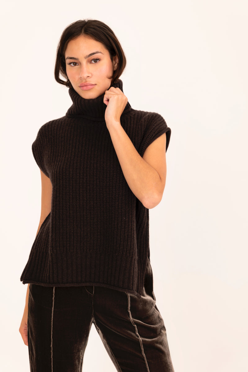 Woman wearing a brown sleeveless ribbed knit top against a white background