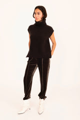 Person wearing a brown sleeveless turtleneck and black pants on a white background