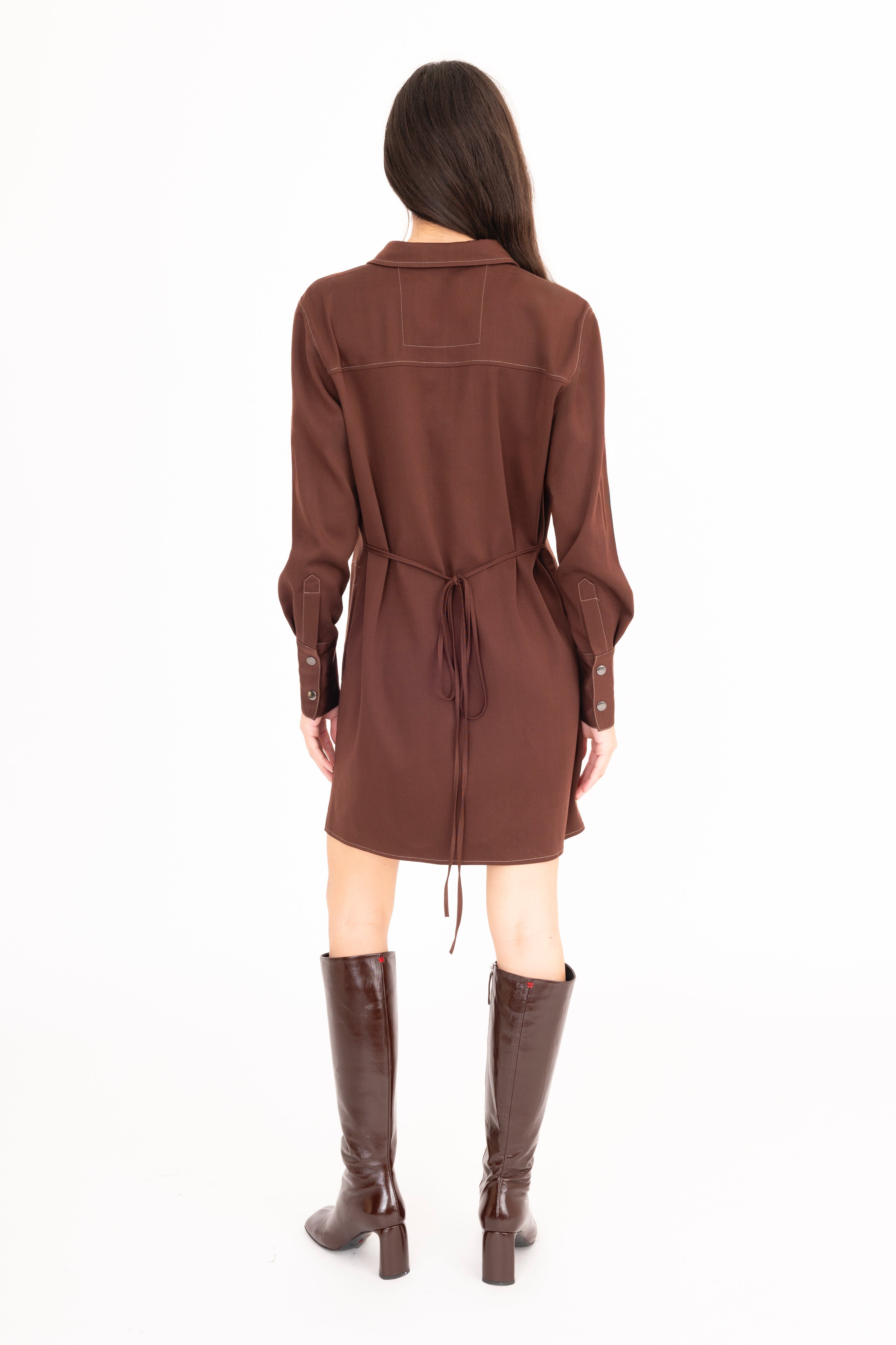 Woman wearing a brown dress with a belt and matching knee-high boots on a white background