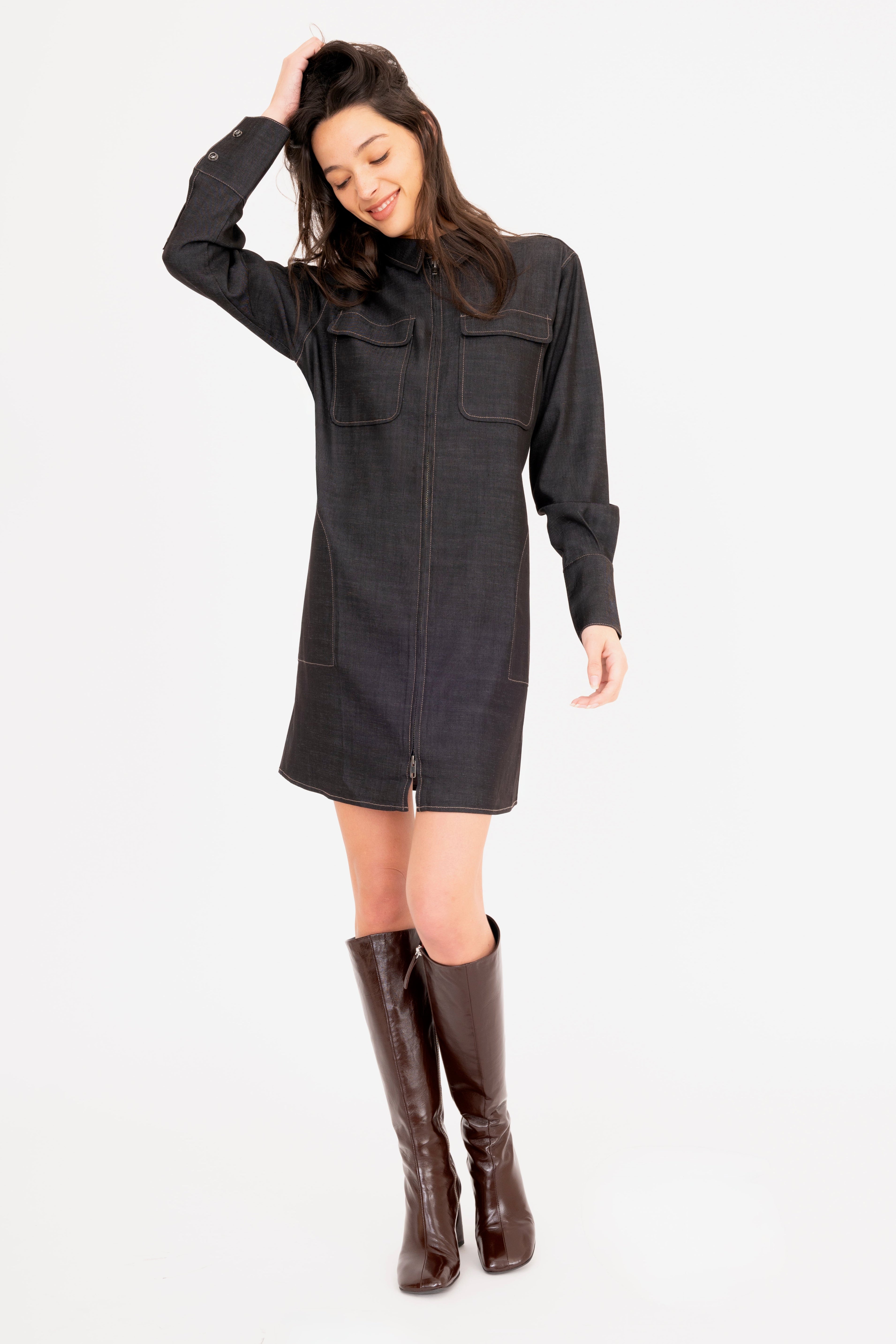 Woman wearing a dark gray dress with long sleeves and brown knee-high boots on a white background