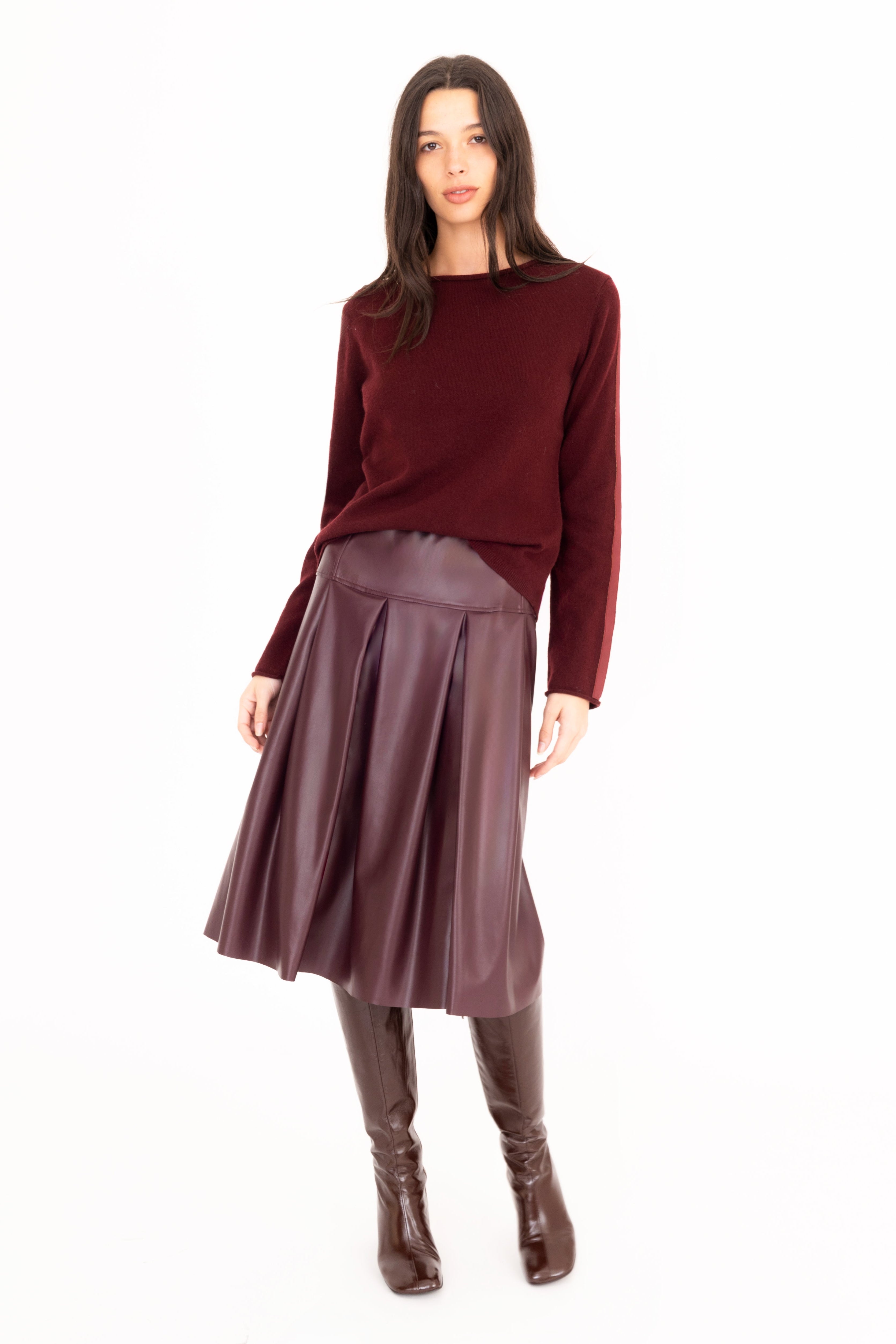 Woman wearing a burgundy sweater and pleated skirt on a white background