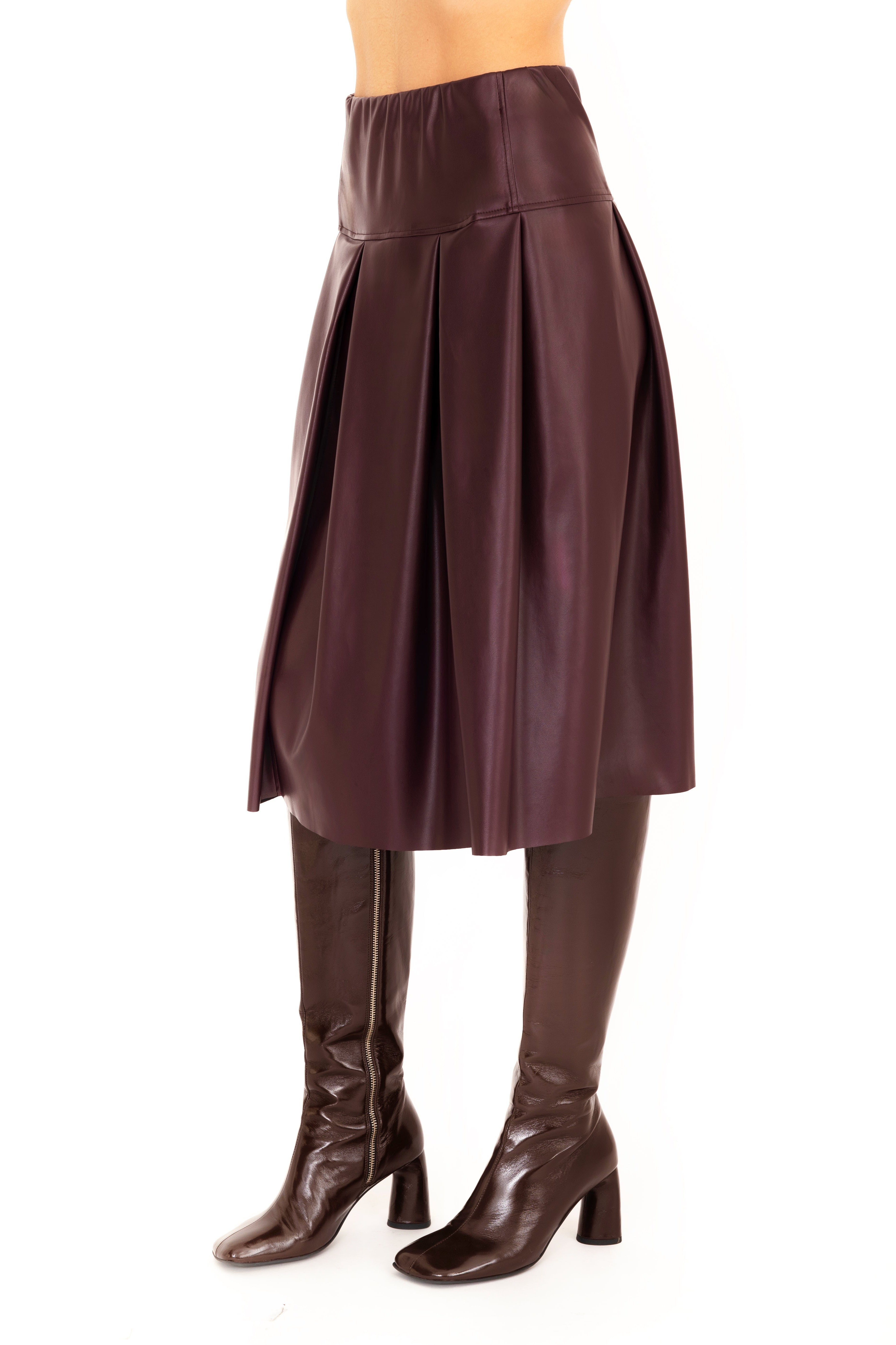 Person wearing a burgundy skirt and brown knee-high boots on a white 