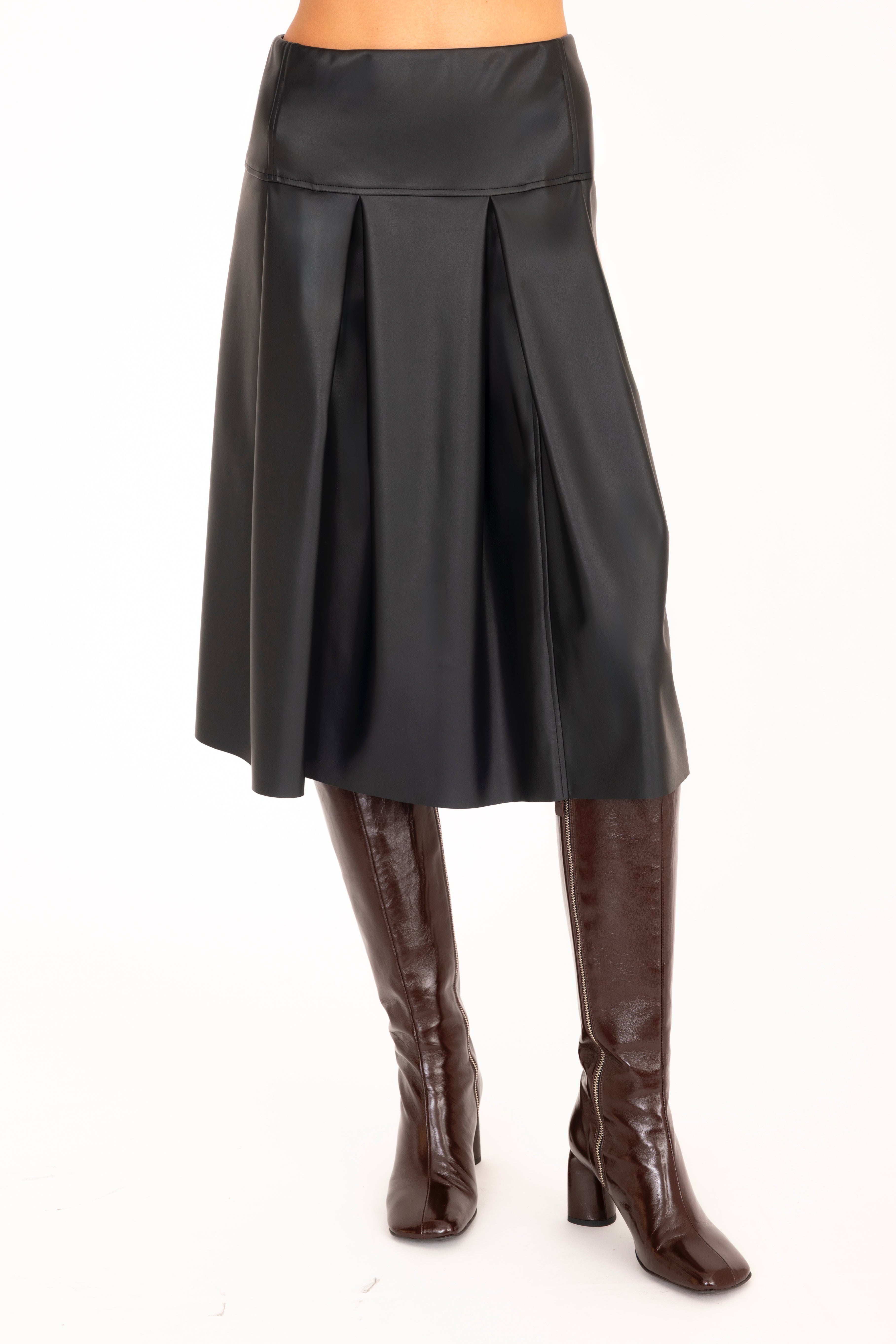 Black pleated skirt worn with brown knee-high boots on a white background