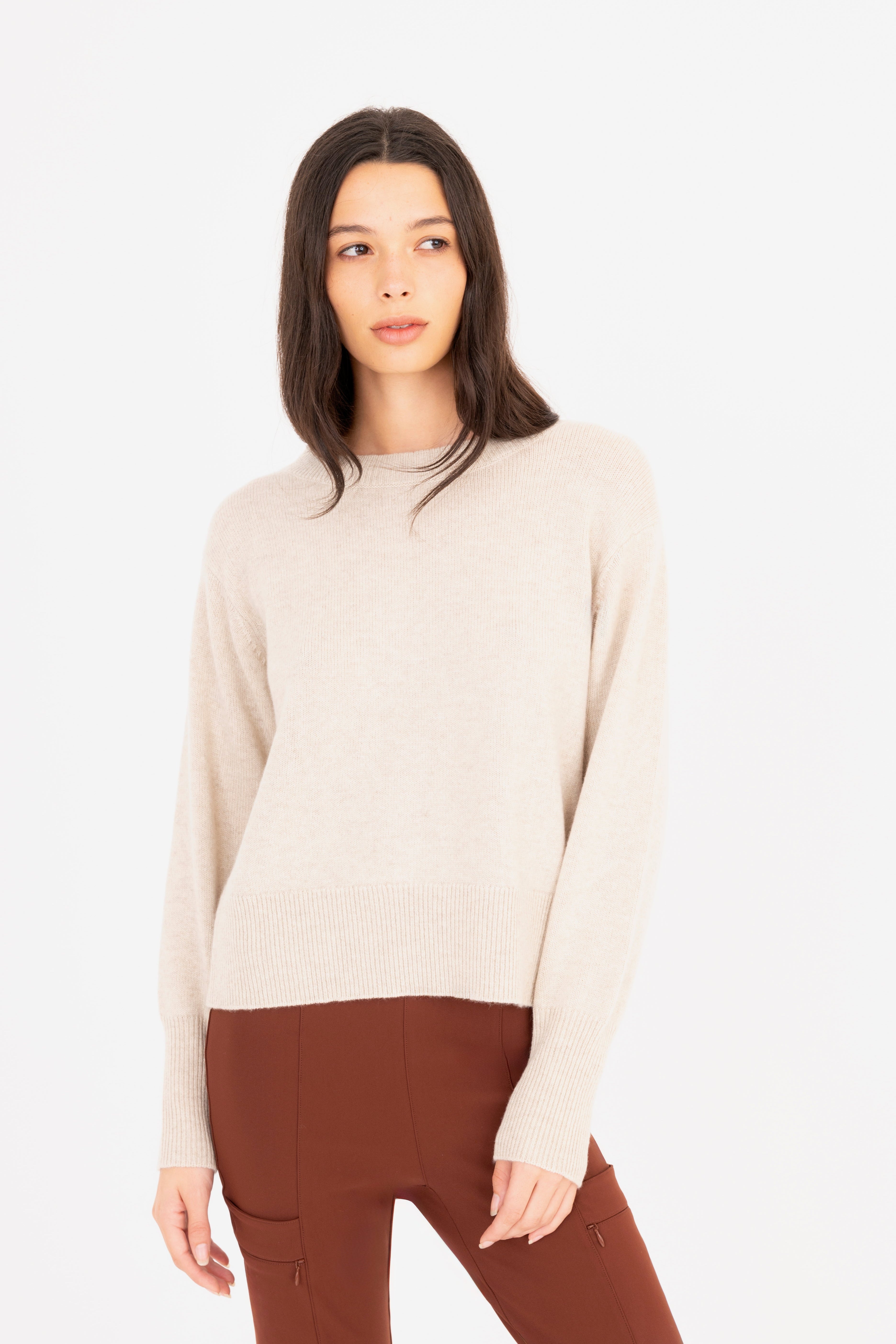 Woman wearing a beige sweater and brown pants on a white background