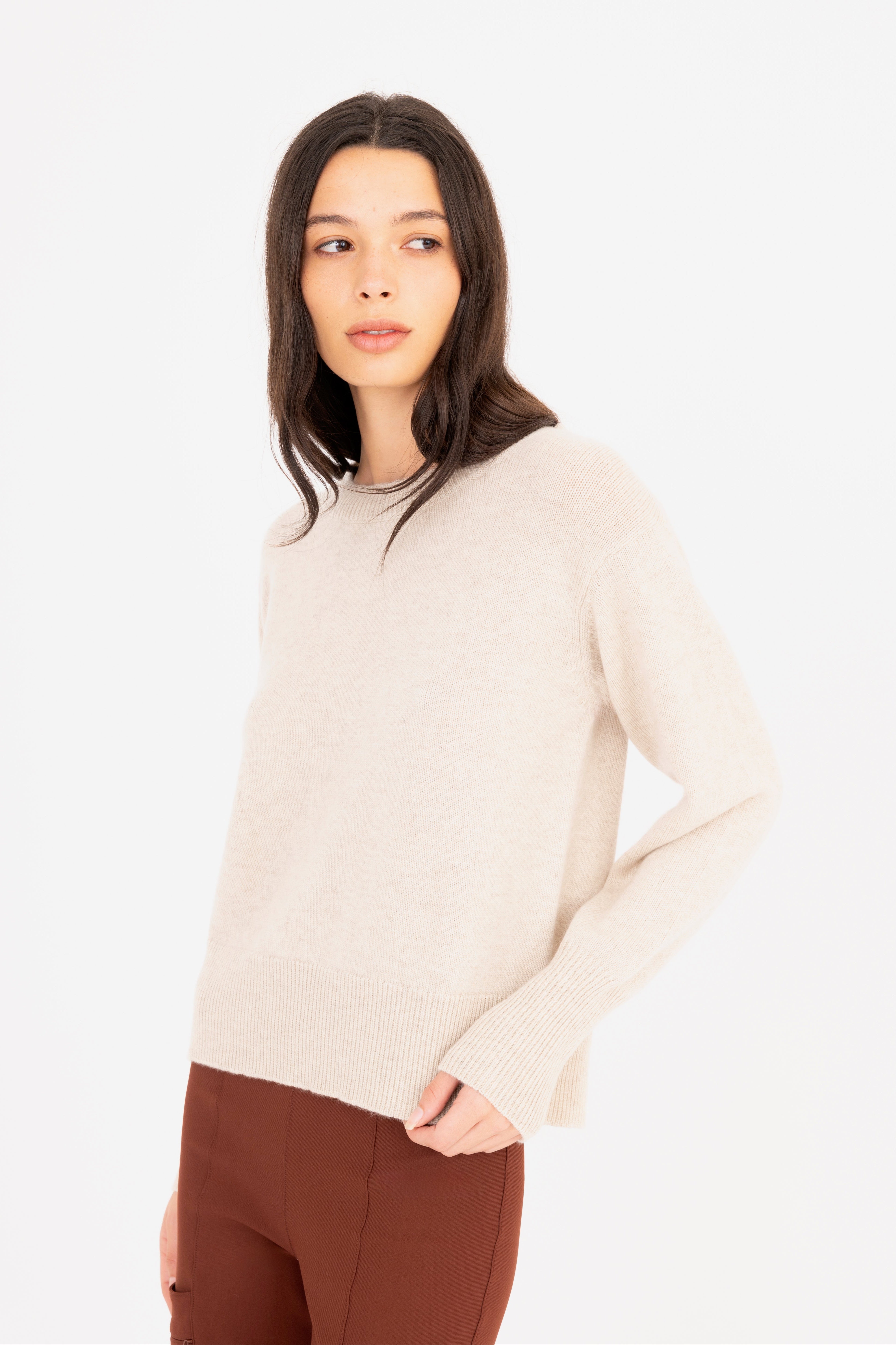 Woman wearing a beige sweater and brown pants on a white background