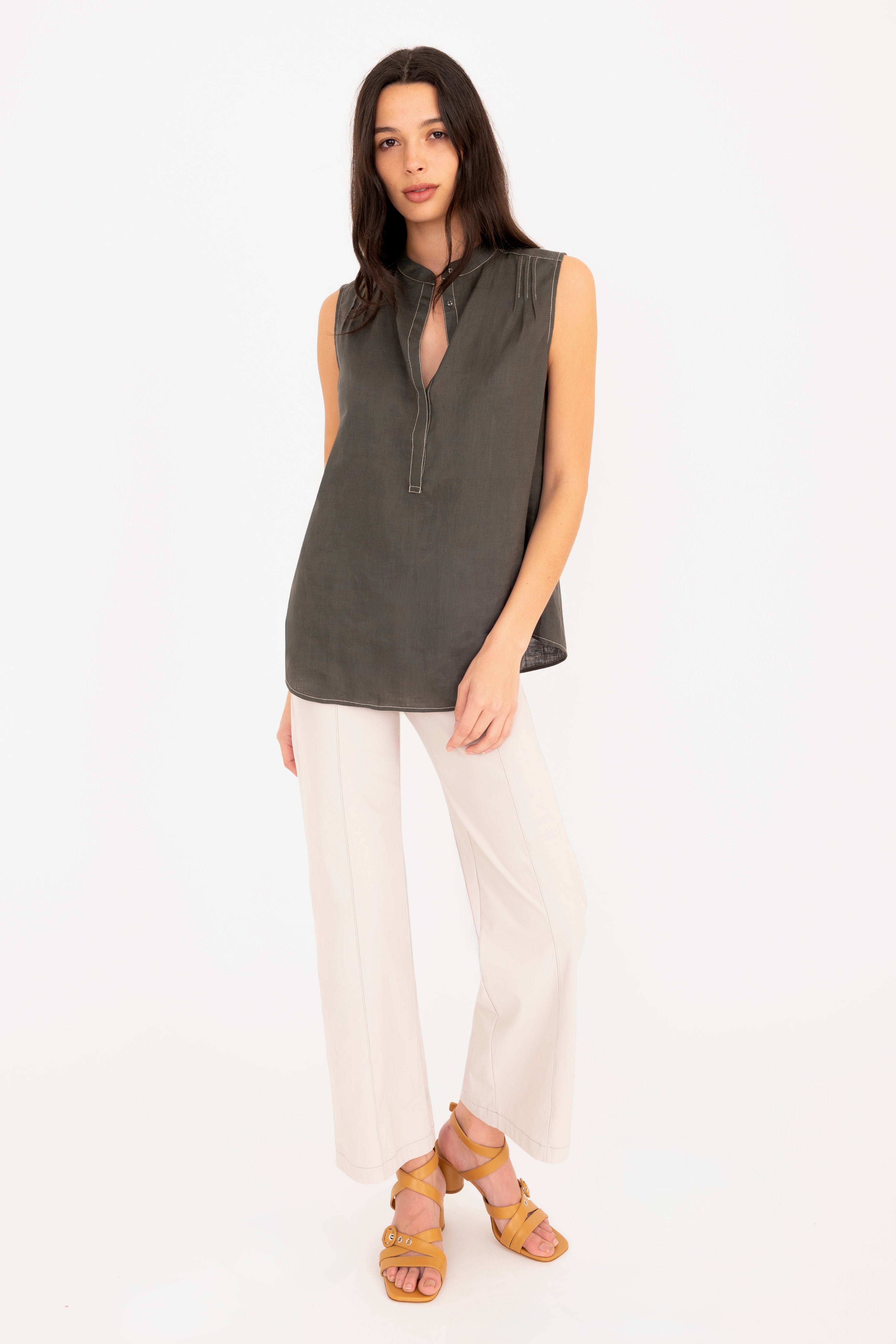 Woman wearing a sleeveless dark green top and beige pants on a white background