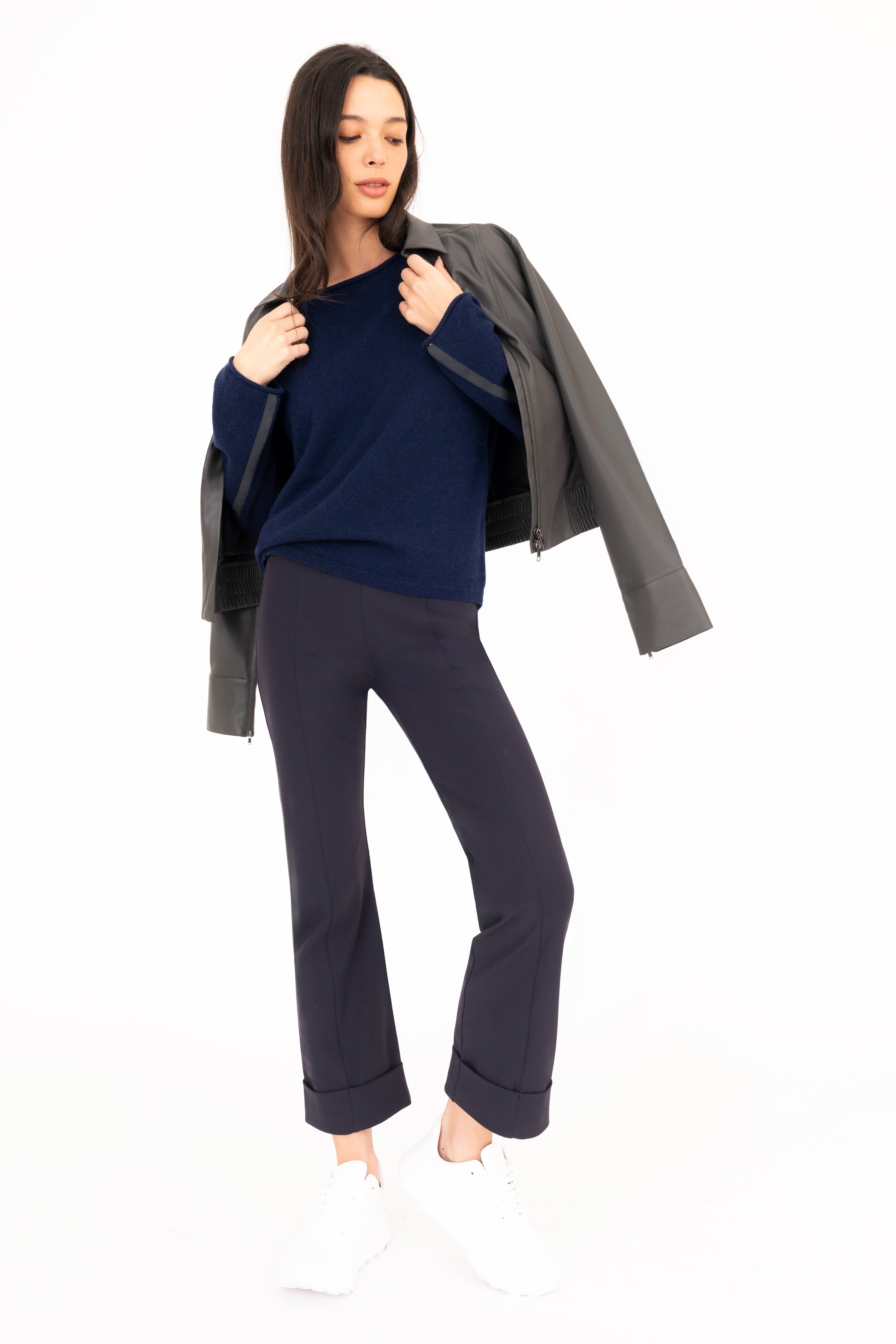 Woman wearing a navy sweater and gray pants with a gray jacket on a white background