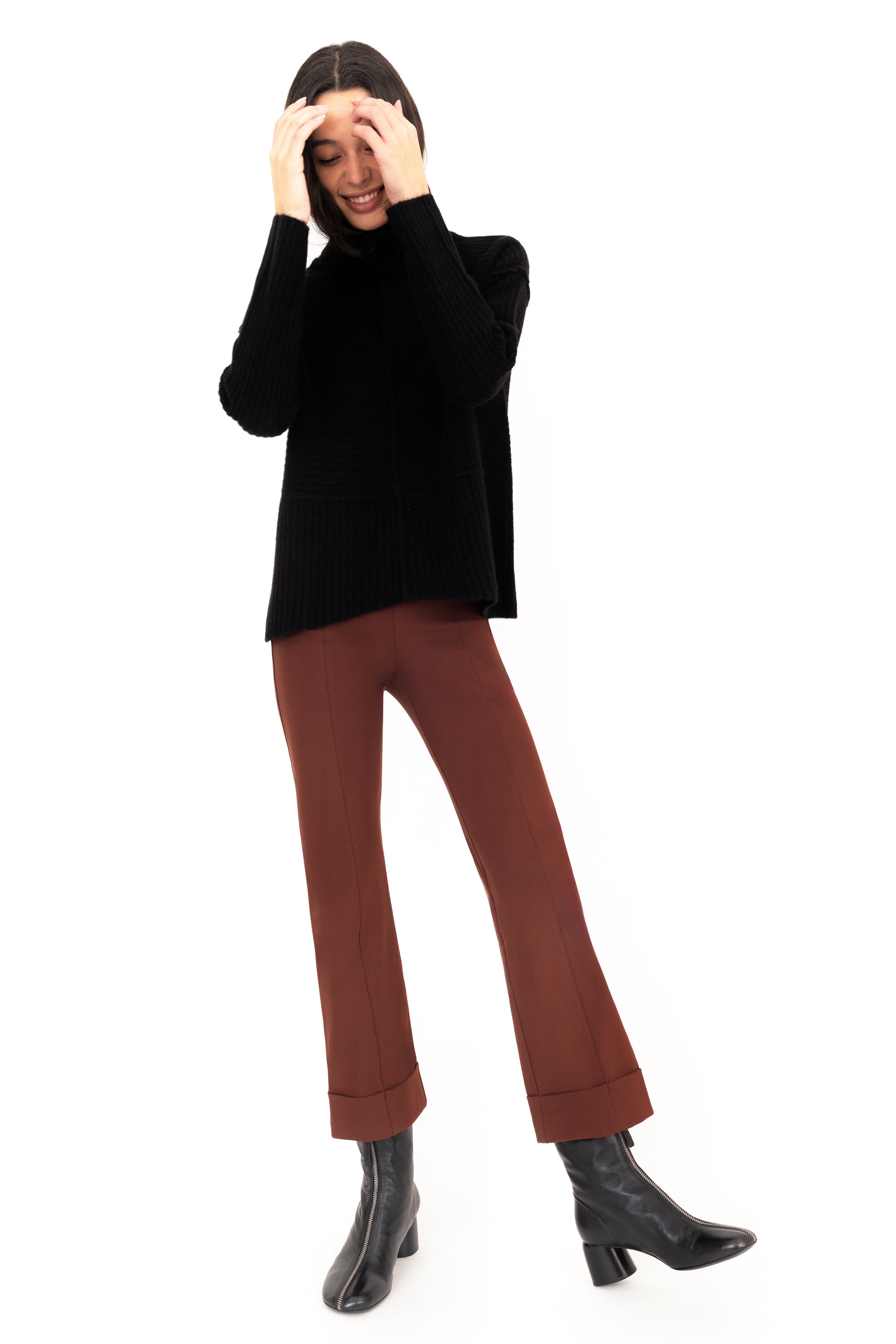 Woman wearing a black sweater and brown pants on a white background