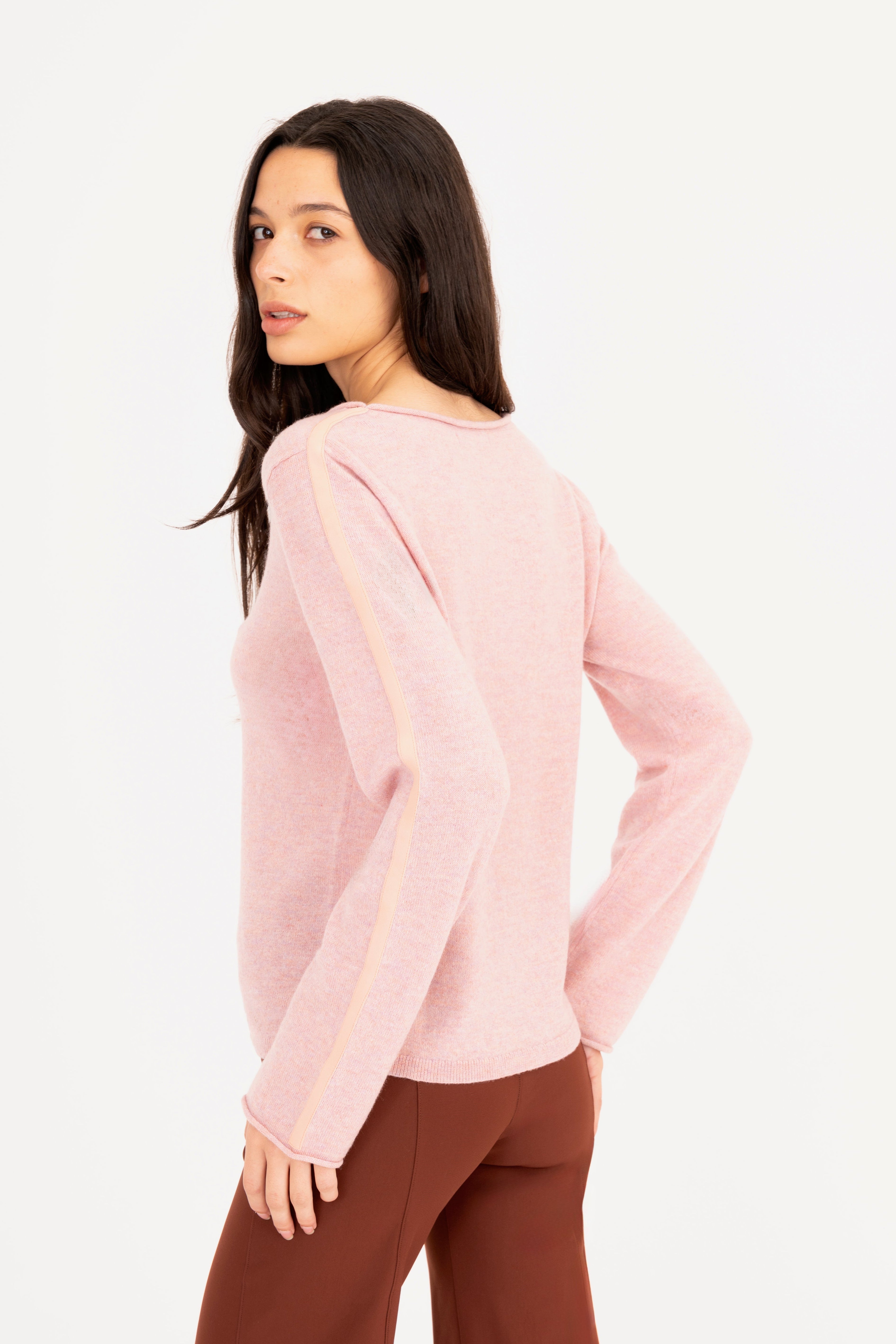 Woman wearing a light pink sweater and brown pants on a white background