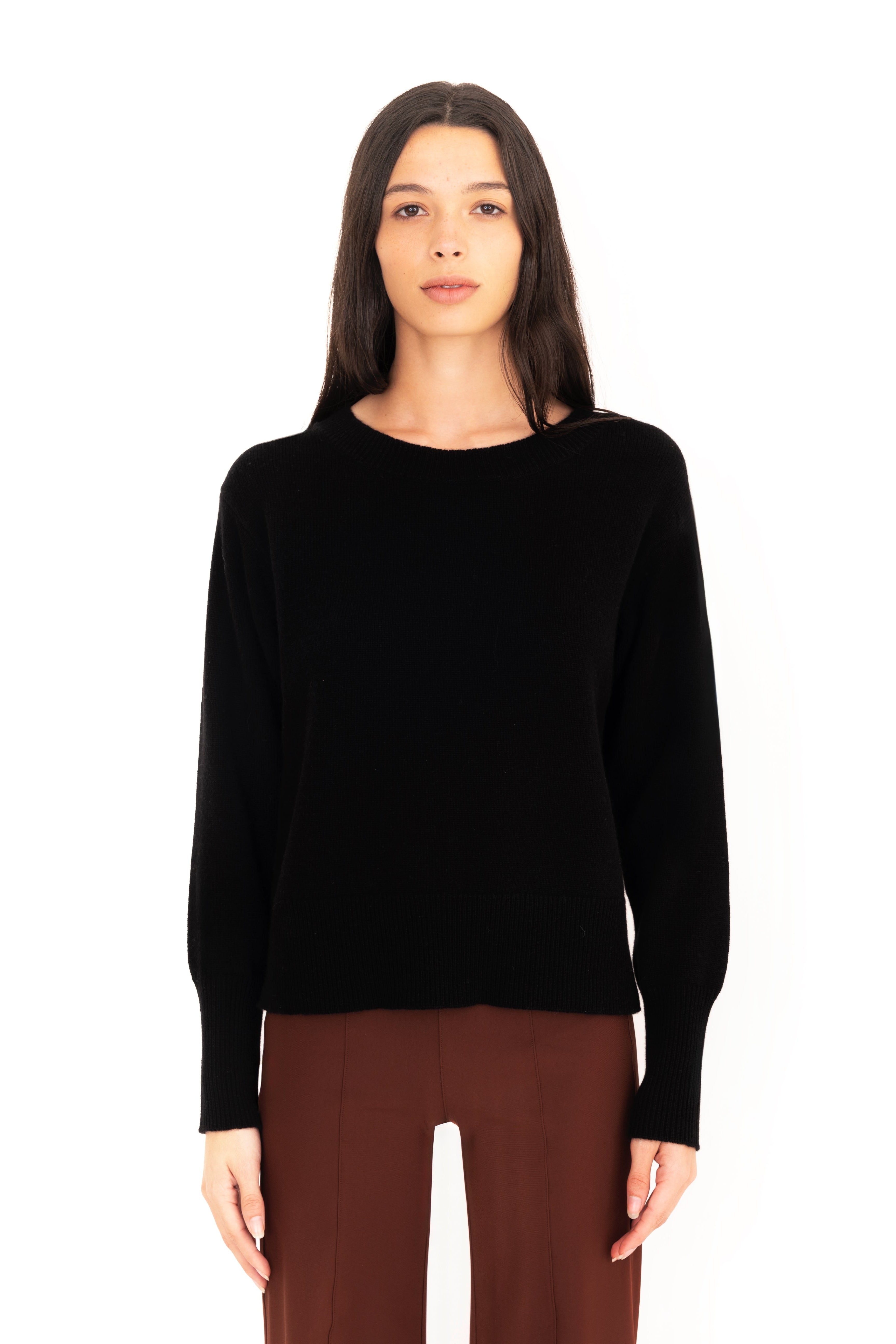 Woman wearing a black long-sleeve top and brown pants on a white background