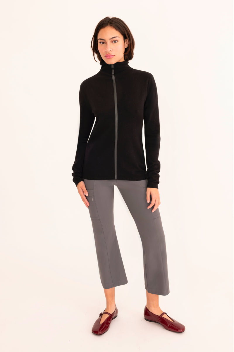 Woman wearing a black zip-up jacket and gray pants on a white background