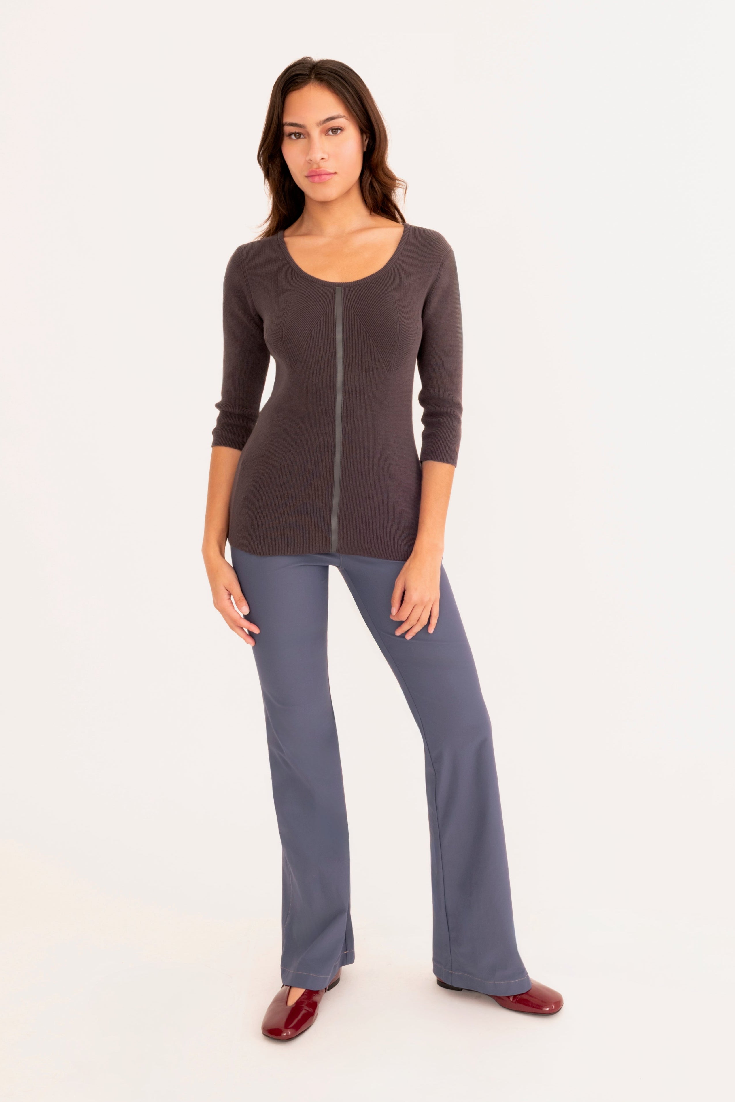 A woman modeling a dark gray three-quarter sleeve knit top and blue pants, standing against a plain white studio background.