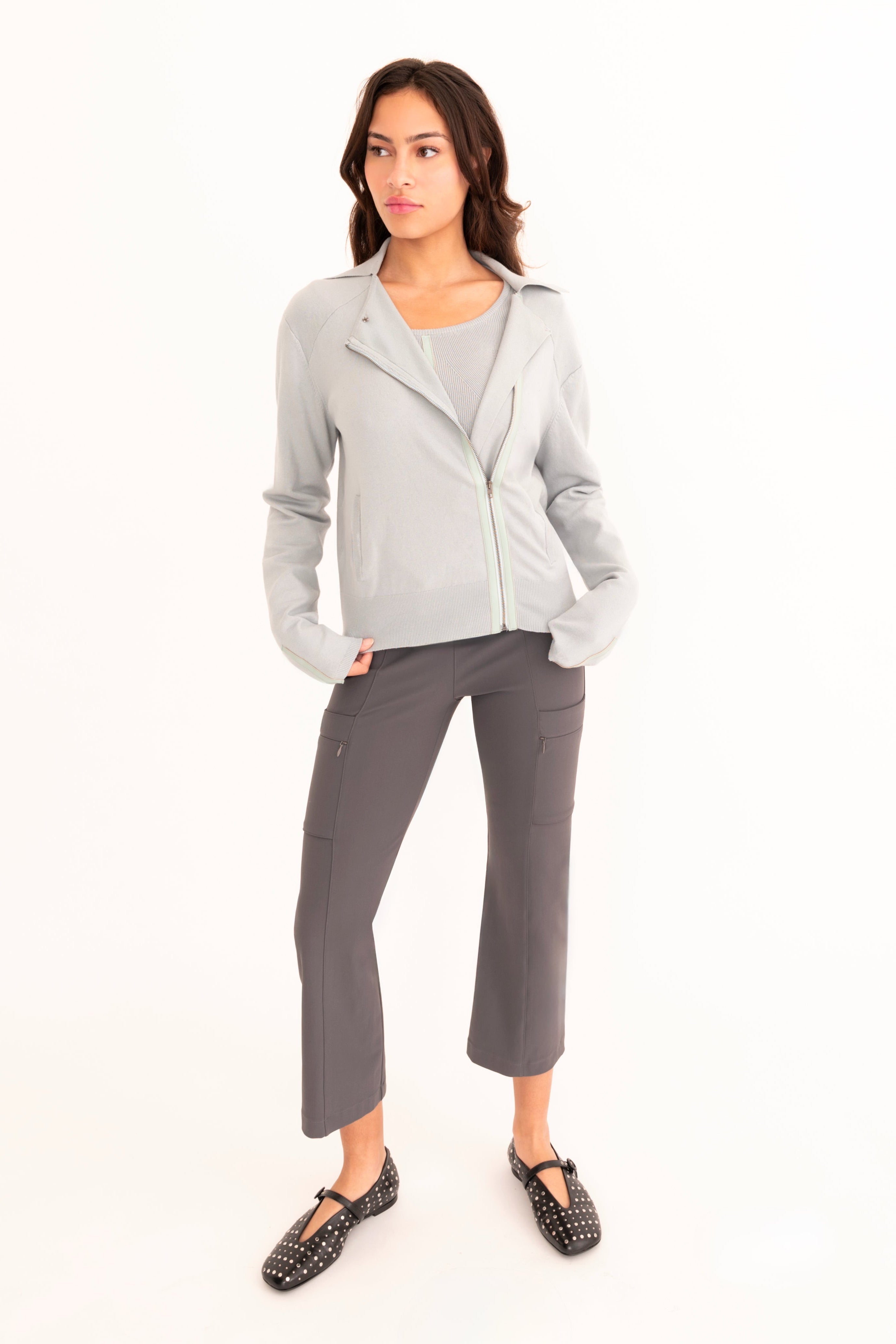 A woman modeling a light blue zip-front cardigan over a matching blue top, paired with dark gray cropped pants, against a plain white studio background.