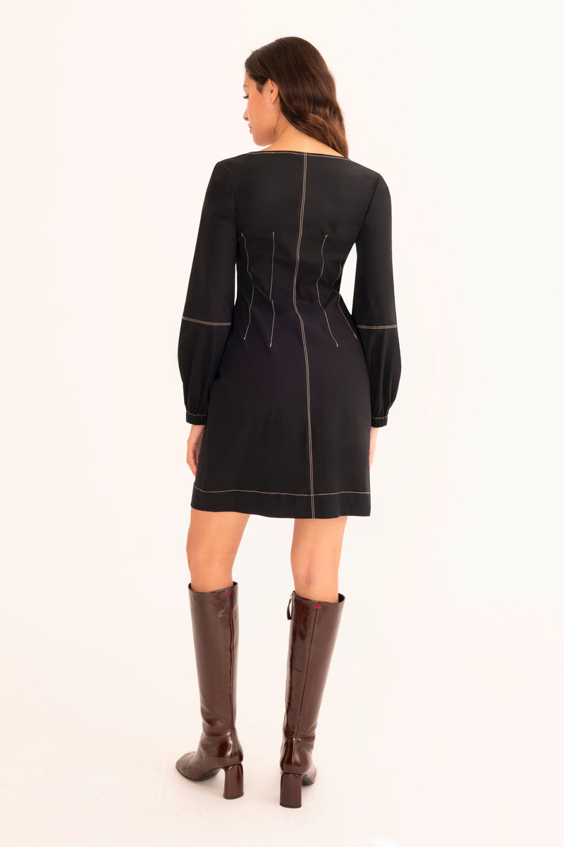 Woman wearing a black dress with white stitching and brown knee-high boots on a white background