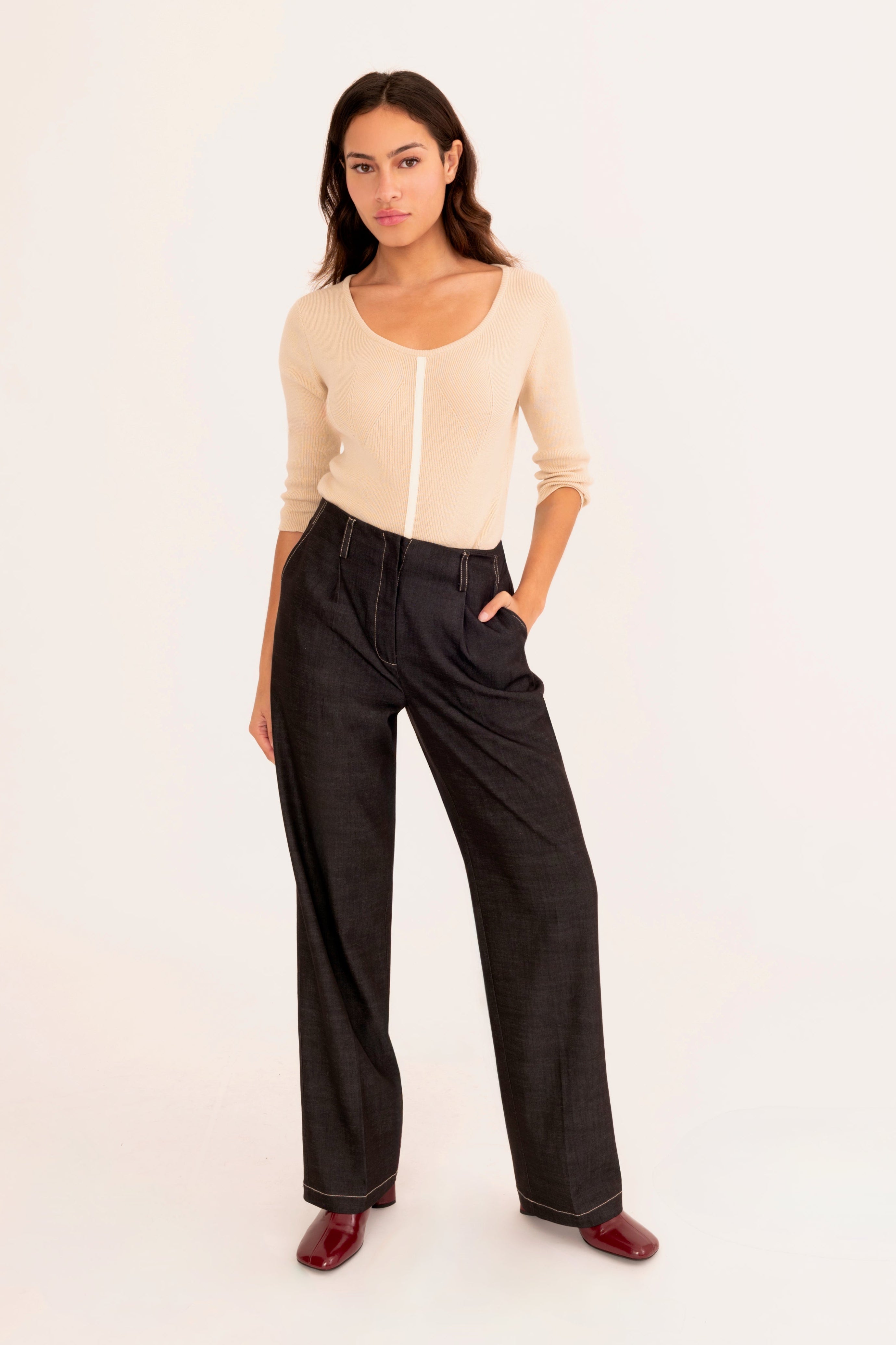 A woman modeling a beige ribbed knit top and black wide-leg pants, standing against a plain white studio background.