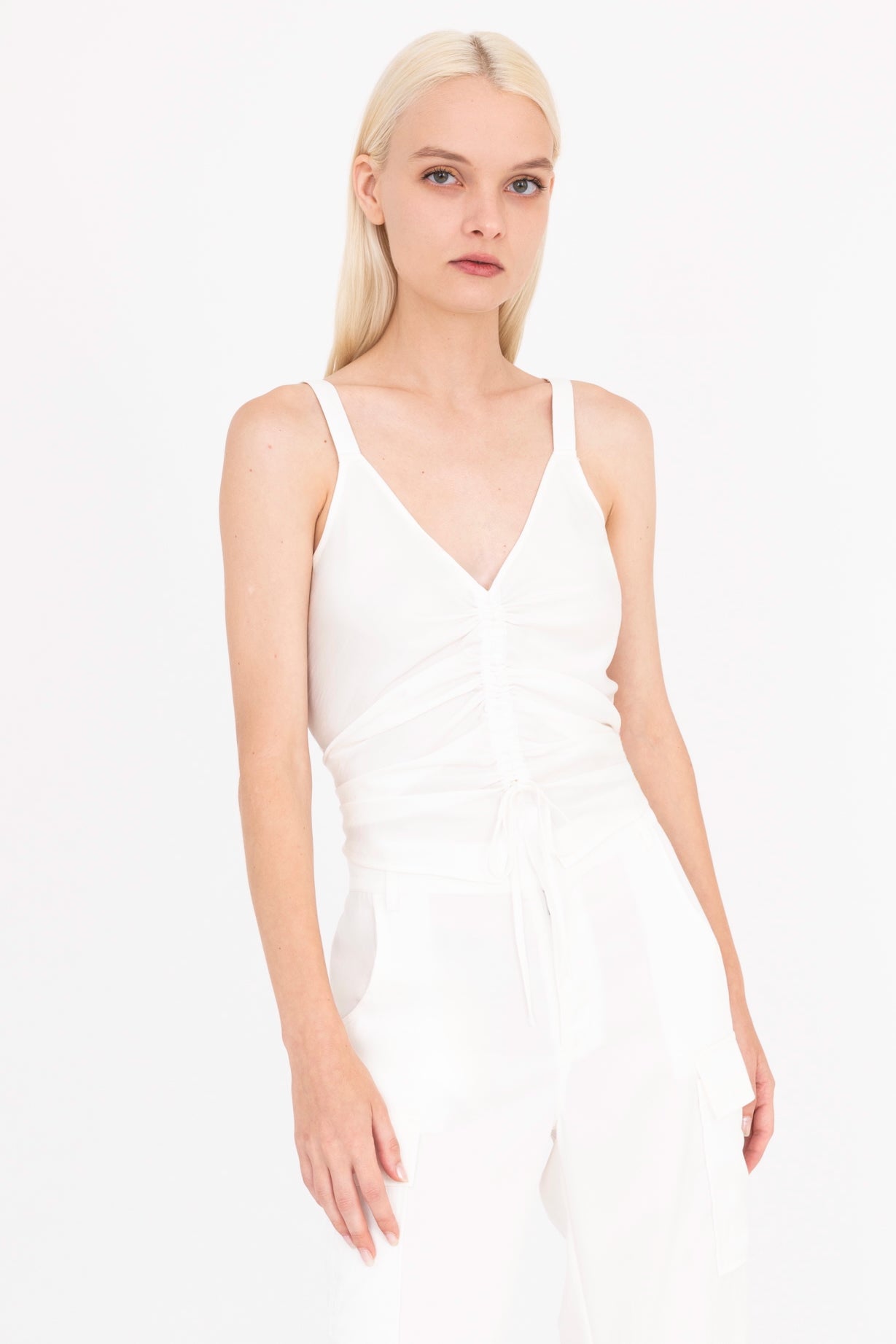 Woman wearing a white sleeveless top with a ruched design on a white background