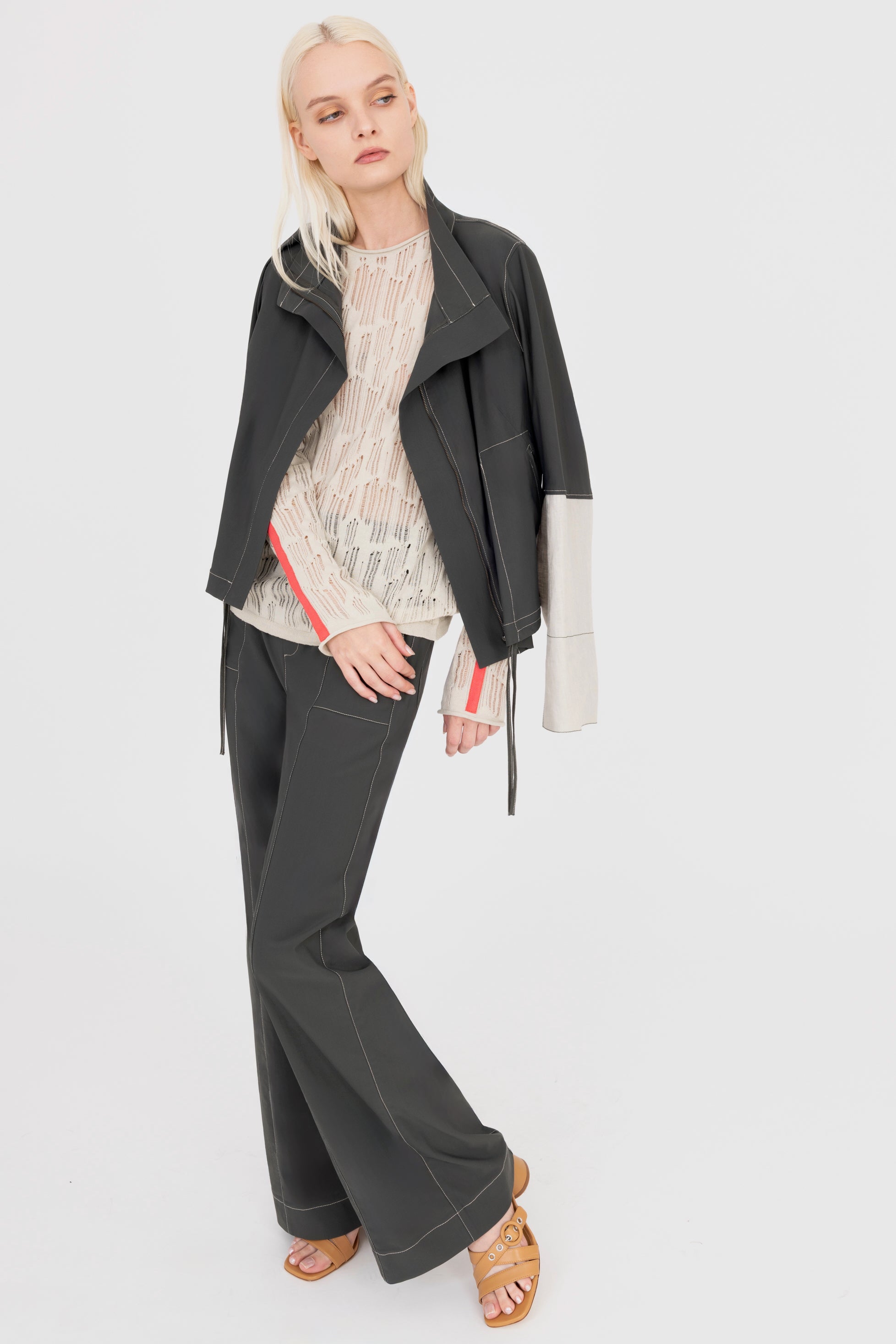 Woman wearing a beige sweater and pine green pants holding a pine green jacket on a white background