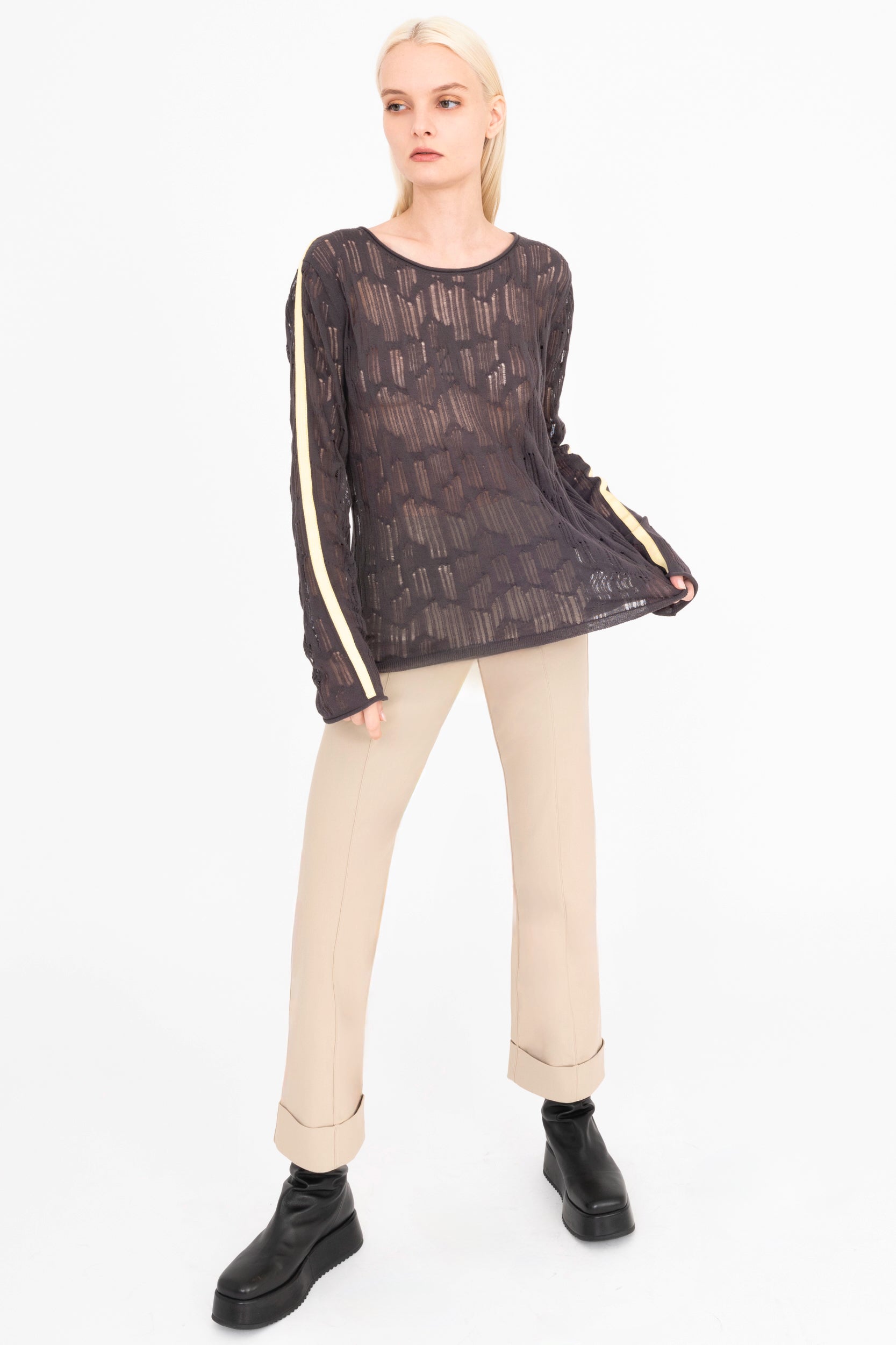 Woman wearing a grey sheer top with cream stripes and beige pants on a white background