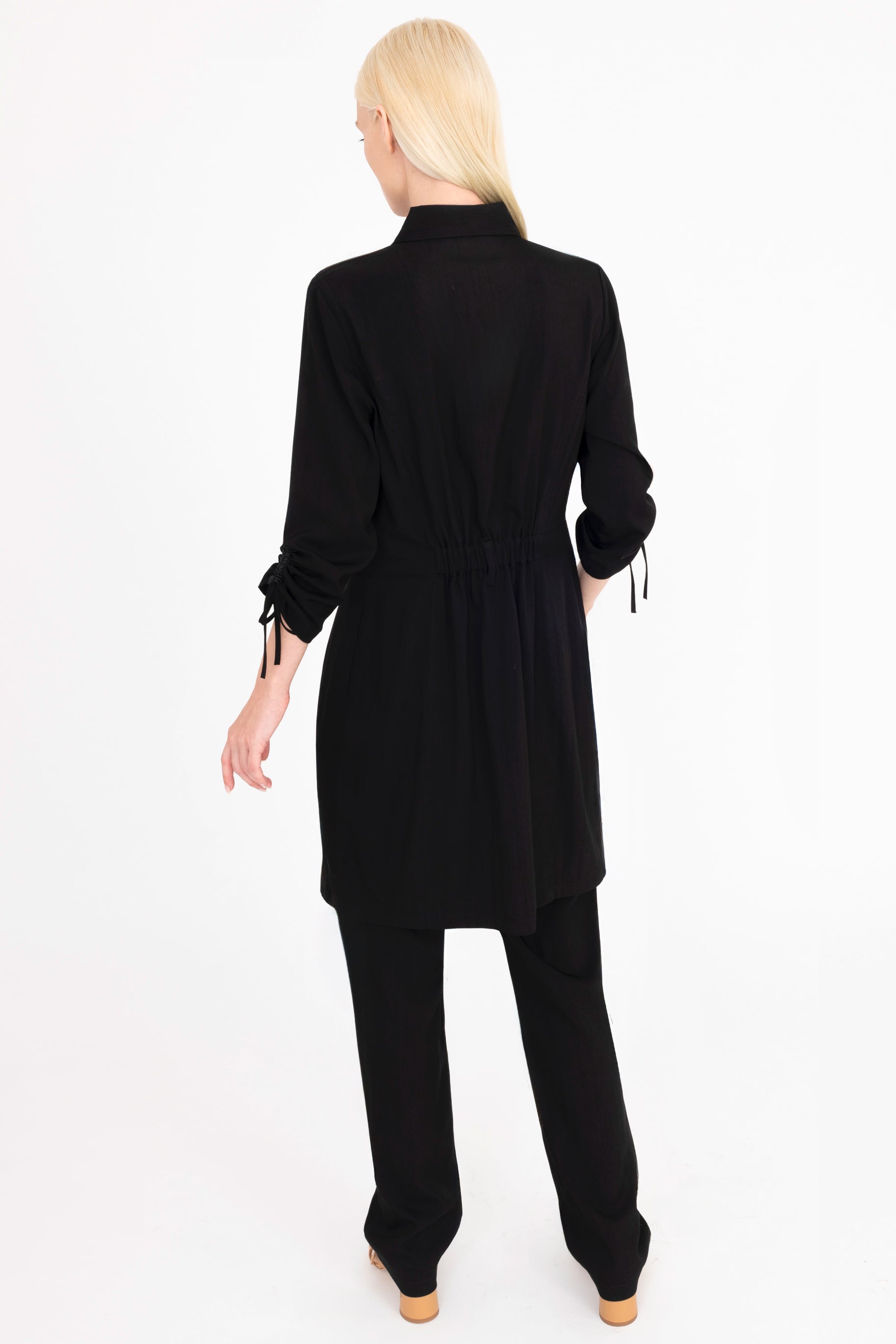 Back view of woman wearing a black dress and pants on a white background