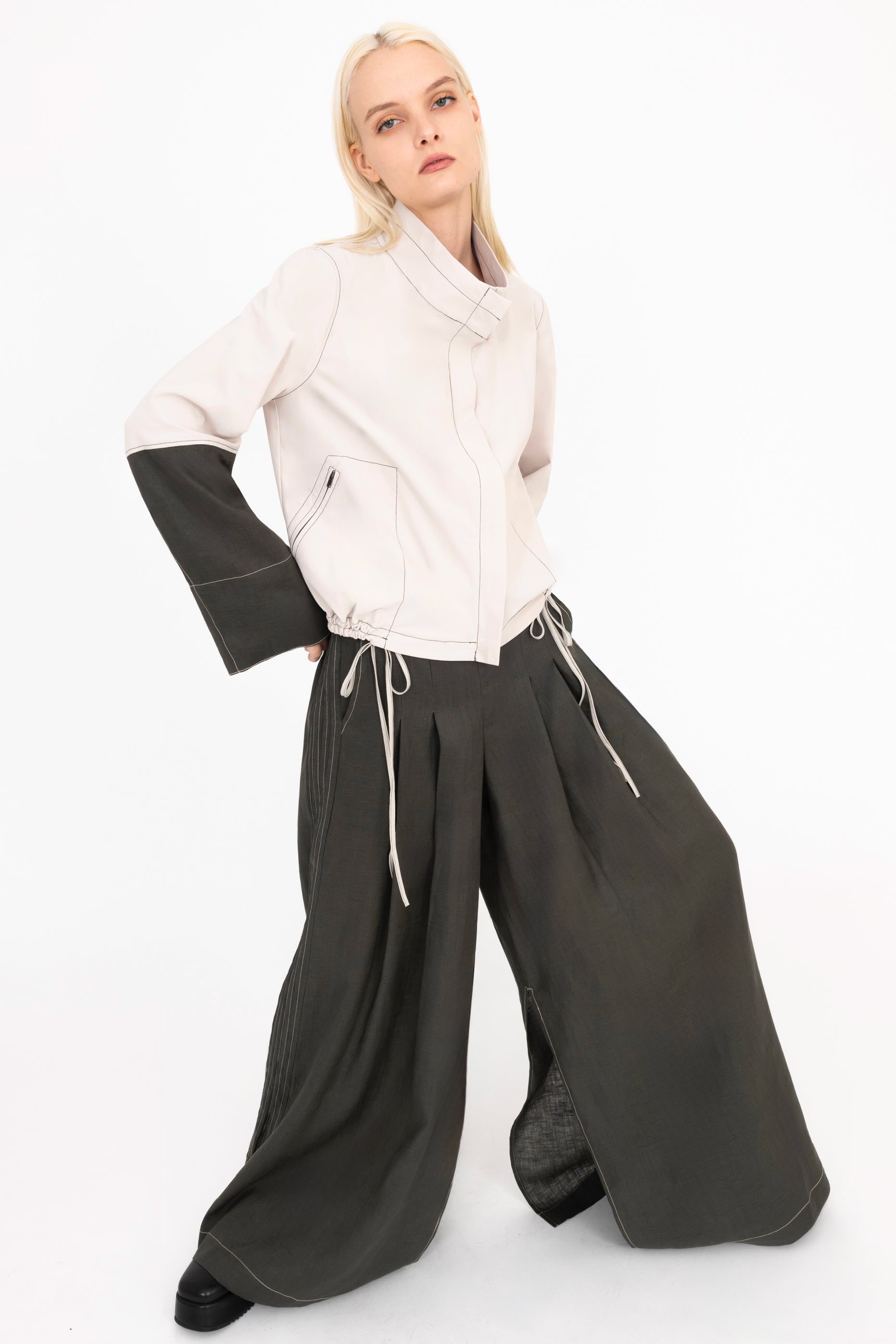 Woman wearing a beige jacket and pine green pants with a white background