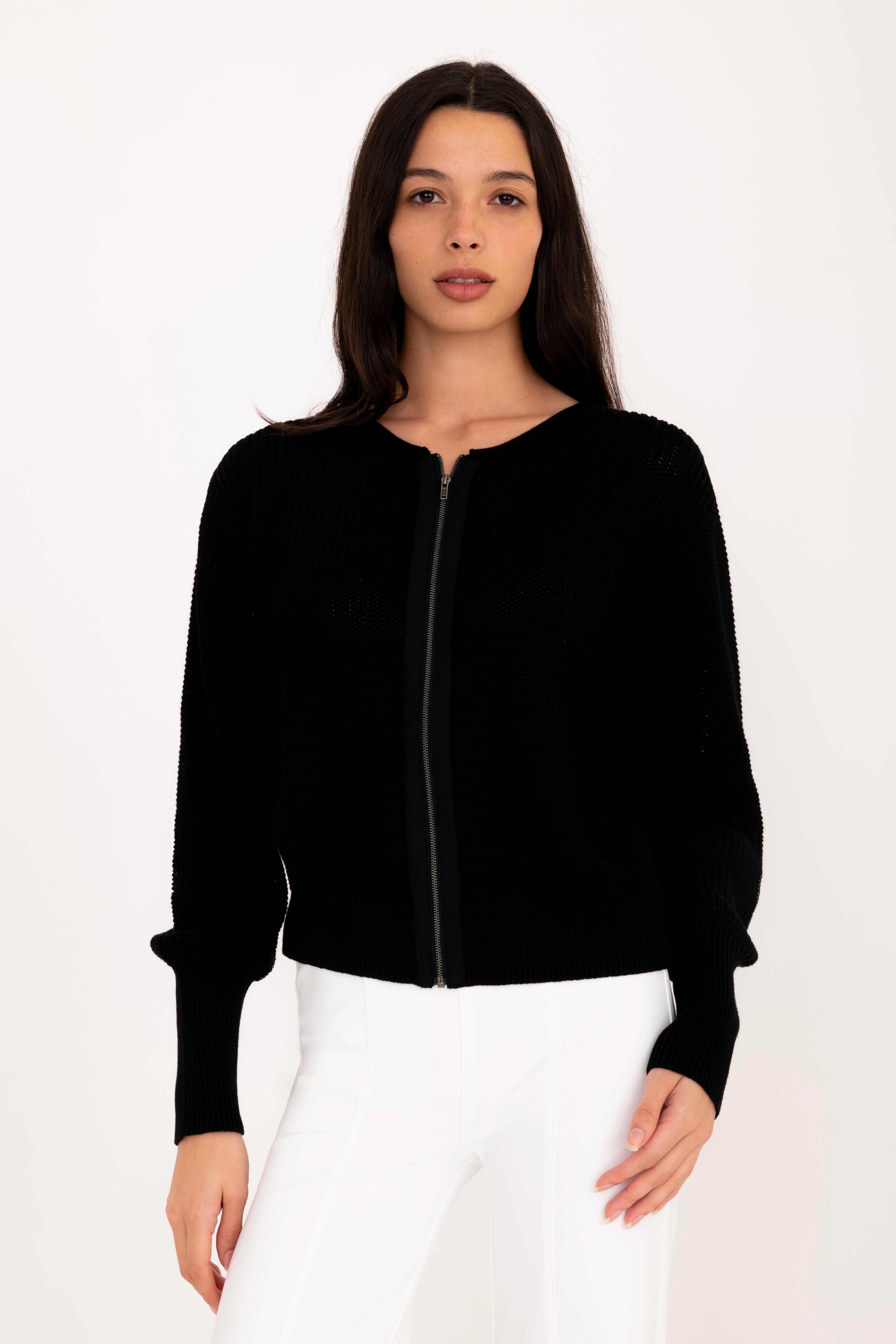Woman wearing a black jacket and white pants on a white background