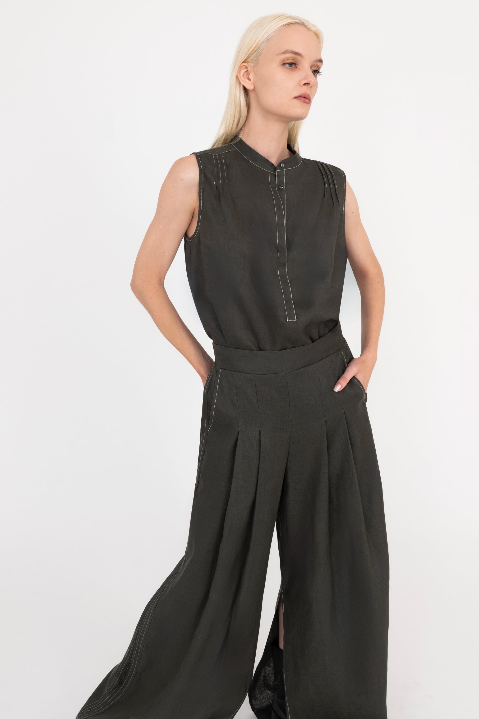 Woman wearing a pine green sleeveless top and wide-leg pants on a white background