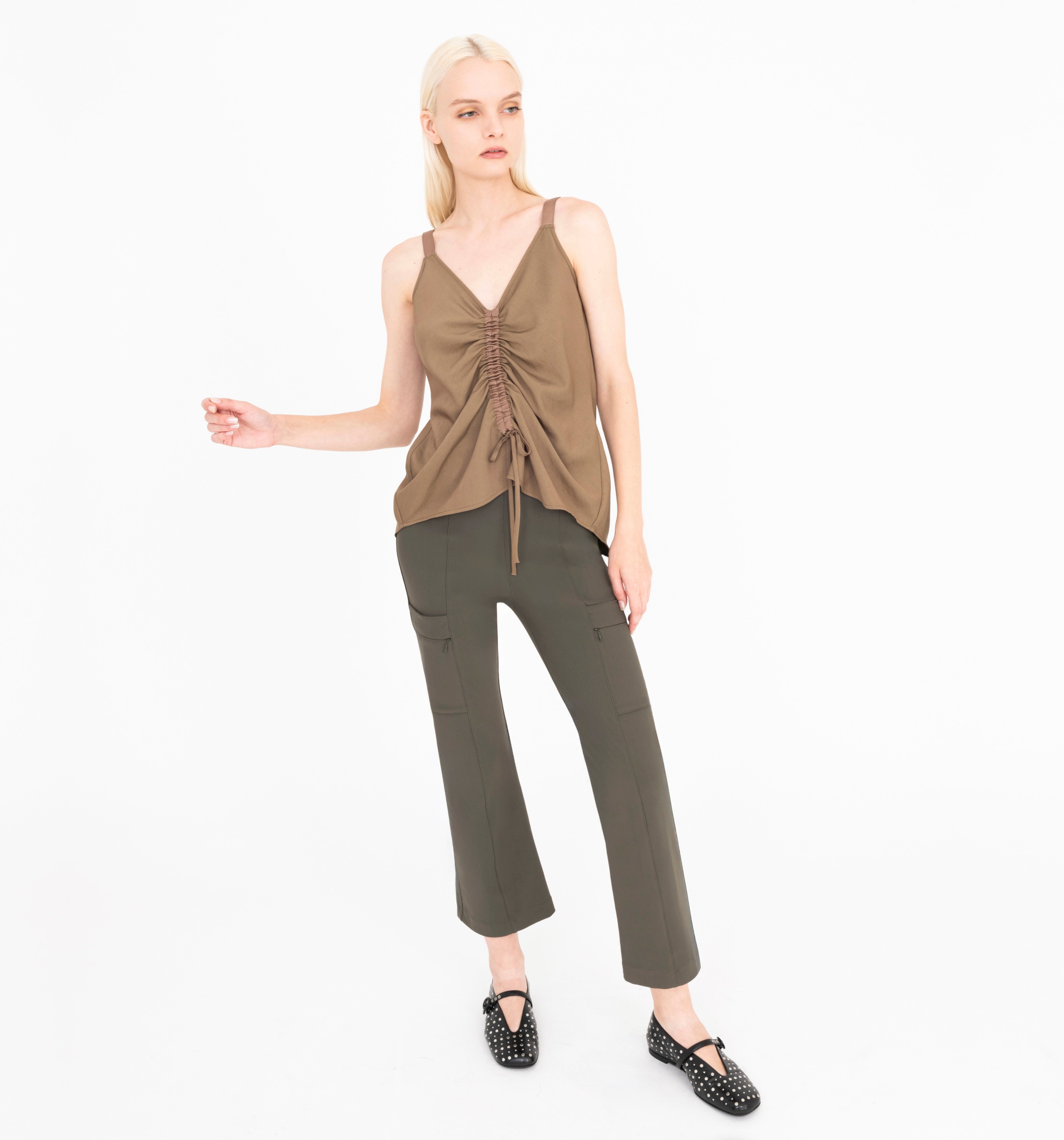 Woman wearing a brown sleeveless top and green pants on a white background