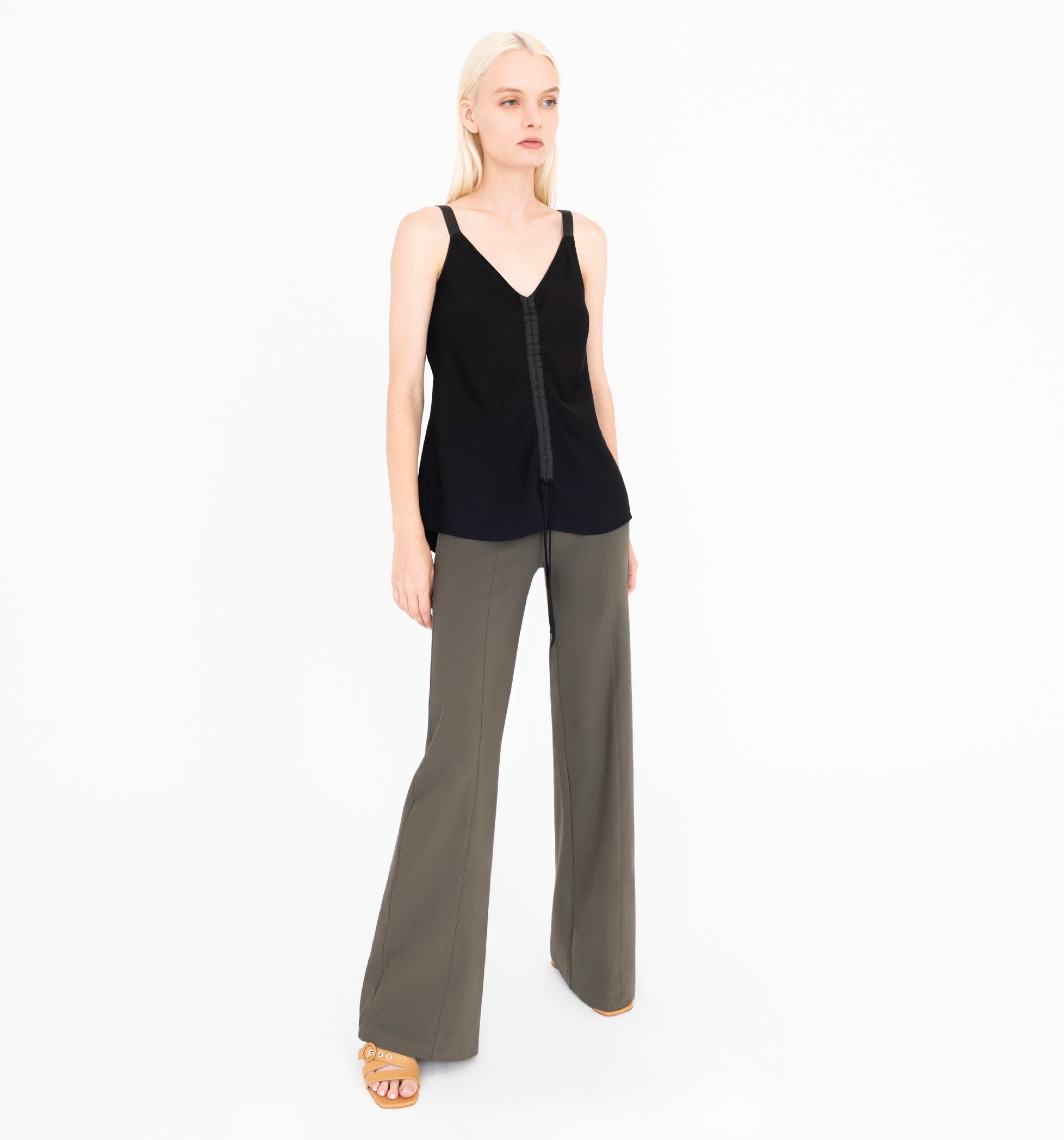 Woman wearing a black sleeveless top and green pants on a white background