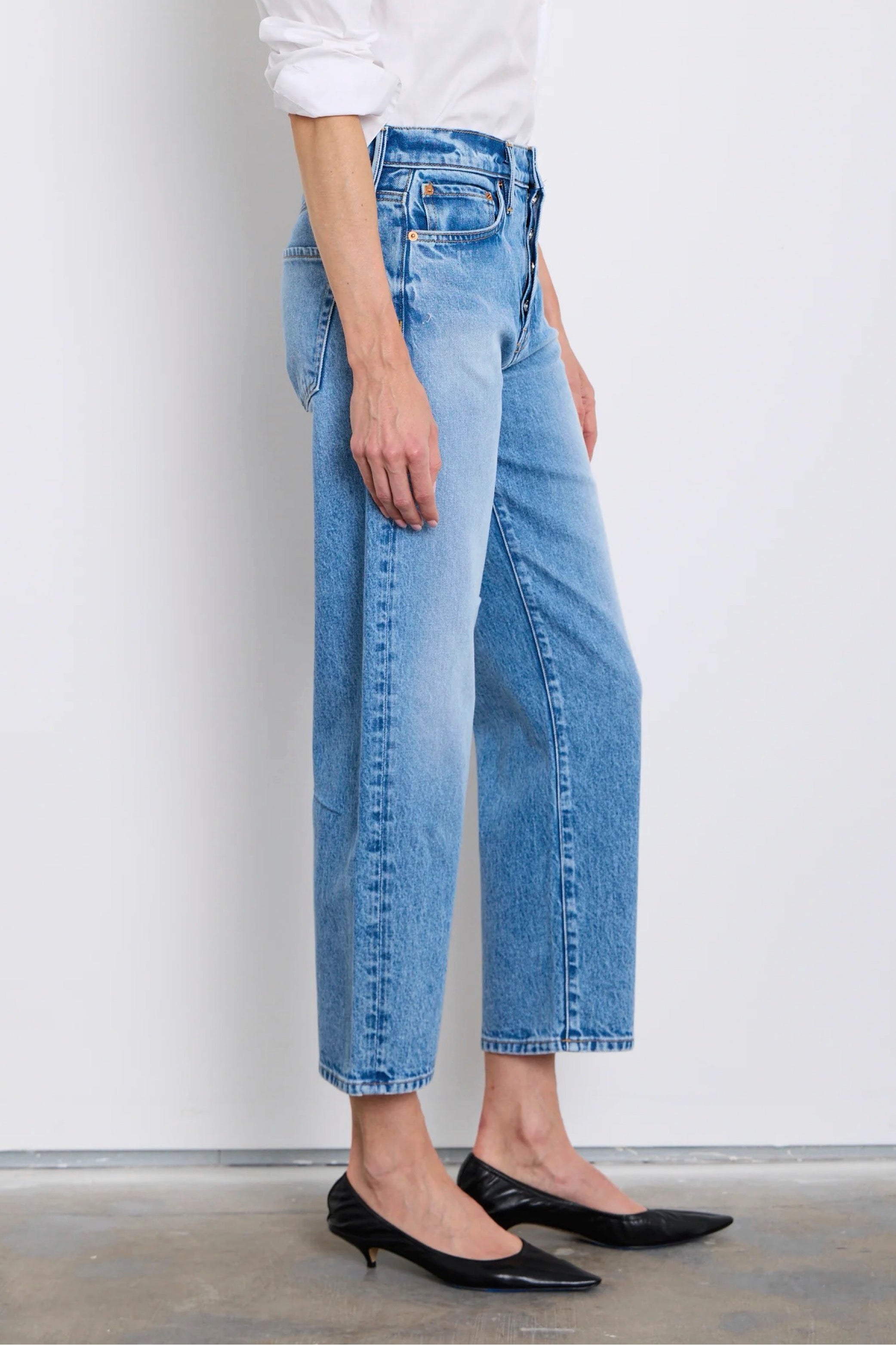 Person wearing light blue jeans and black shoes on a plain background