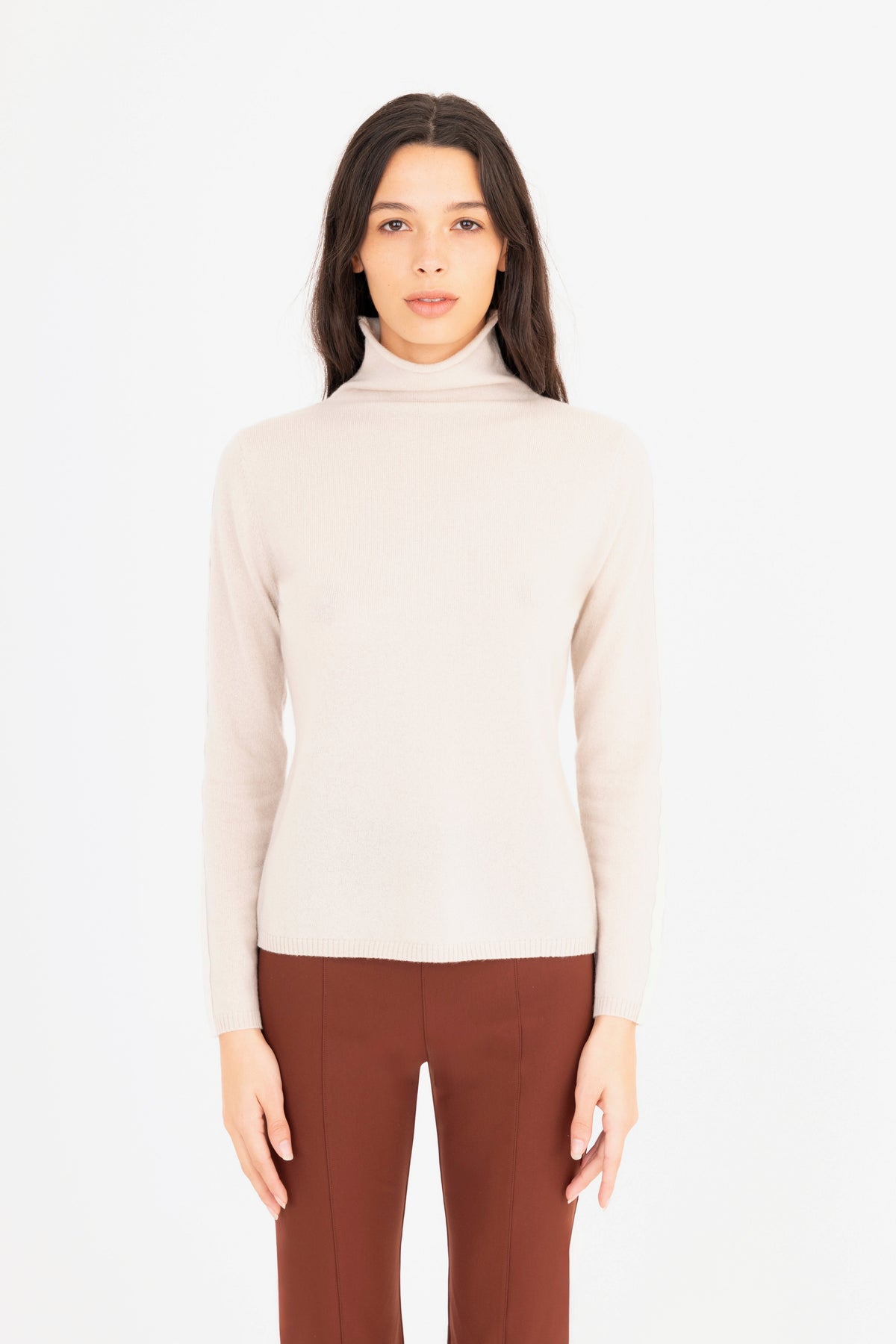 Woman wearing a beige turtleneck sweater and brown pants on a white background