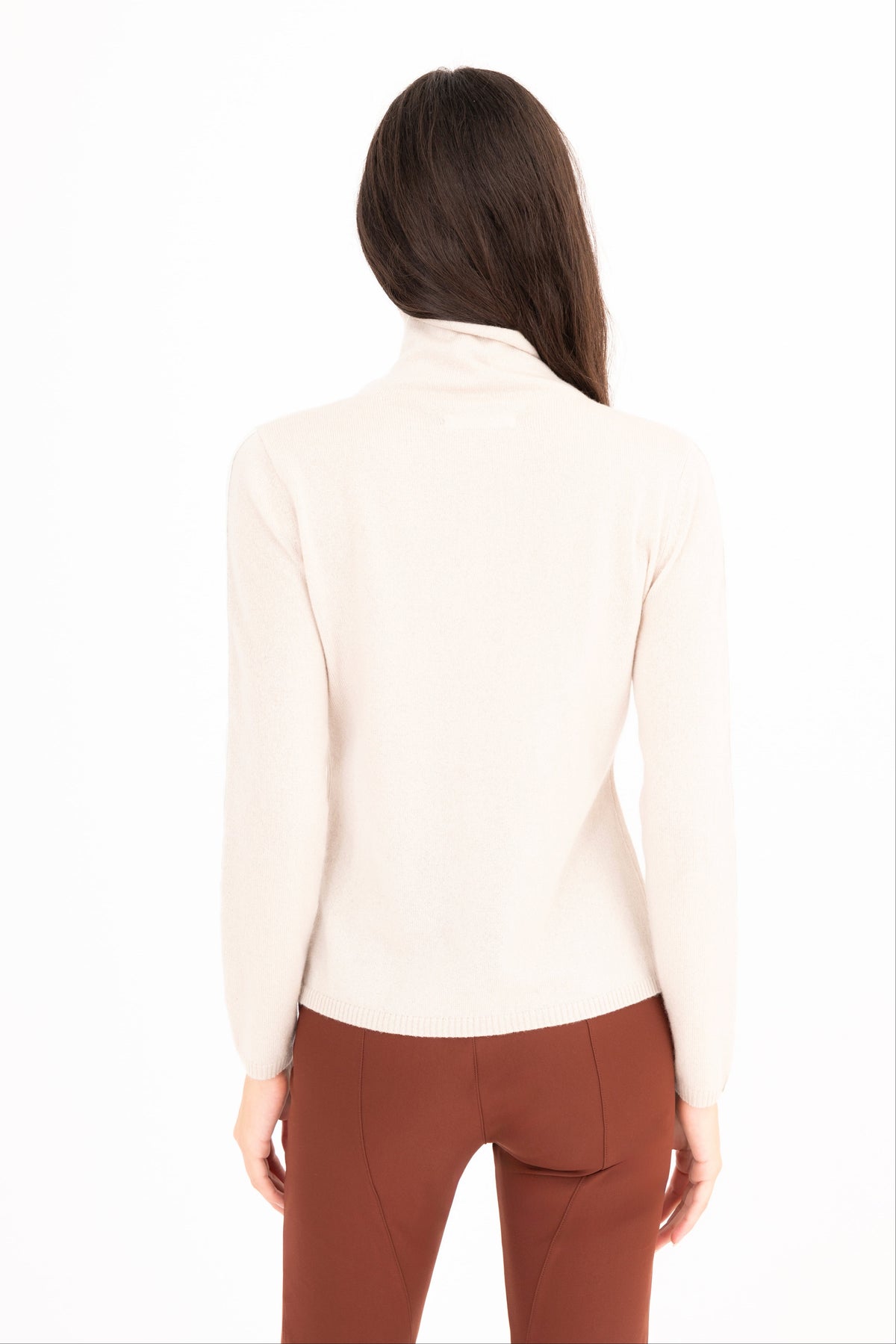 A woman viewed from the back wearing beige long-sleeve mock neck top and brown pants, set against a plain white background.