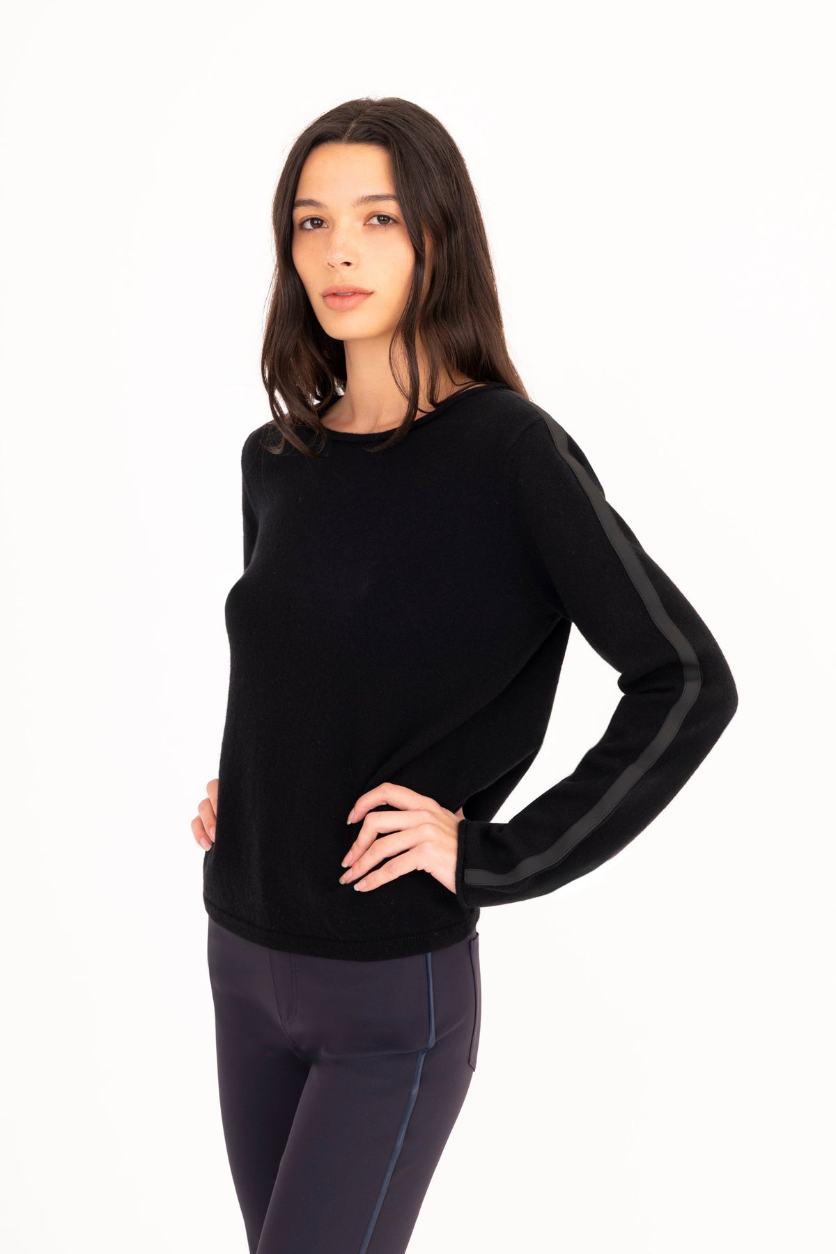A woman modeling a black long-sleeve knit sweater, paired with navy blue pants, against a plain white studio background.