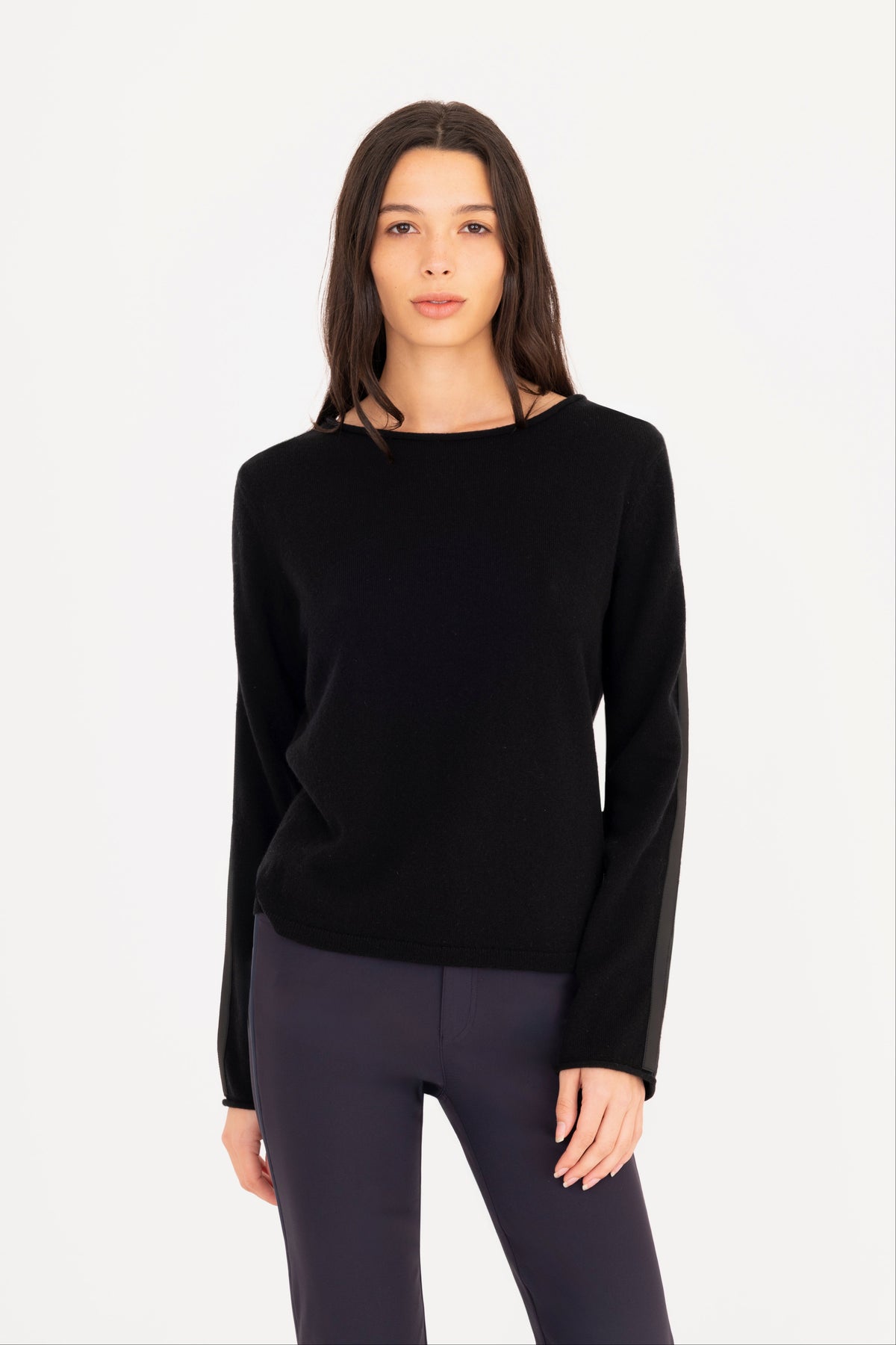 A woman modeling a black long-sleeve knit sweater, paired with navy blue pants, against a plain white studio background.