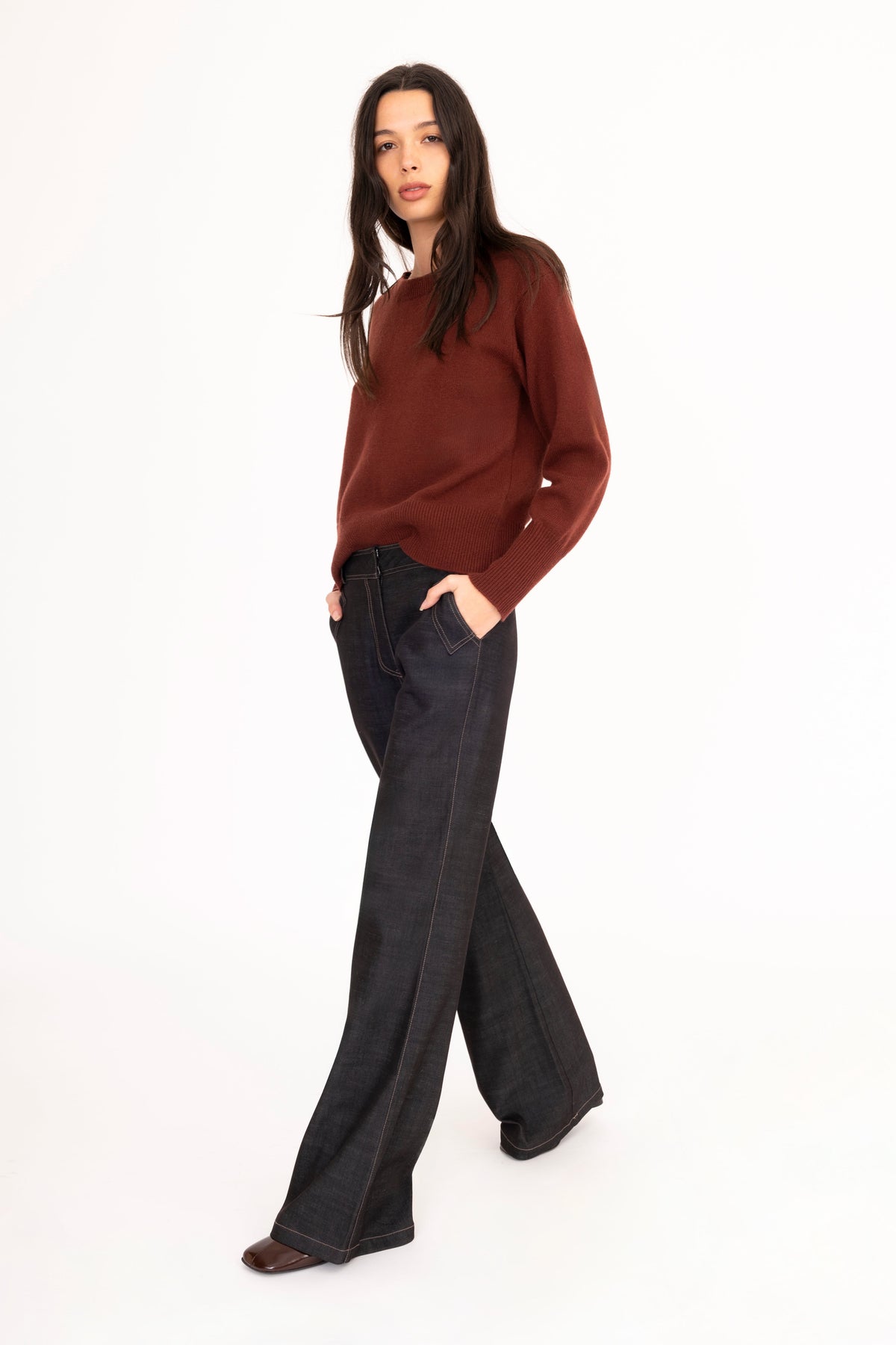 A woman modeling a brown cashmere long-sleeve knit sweater and black flare pants against a plain white studio background.