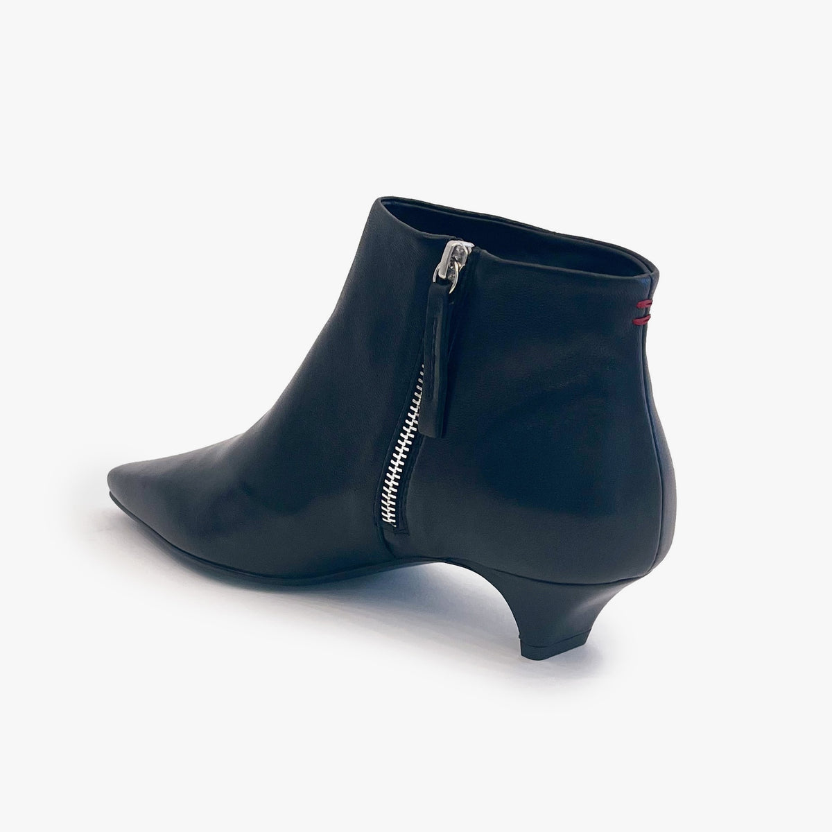 A black leather ankle boot with a pointed toe, low kitten heel, and a silver zipper on the side, shown from a three-quarters rear angle against a white background.