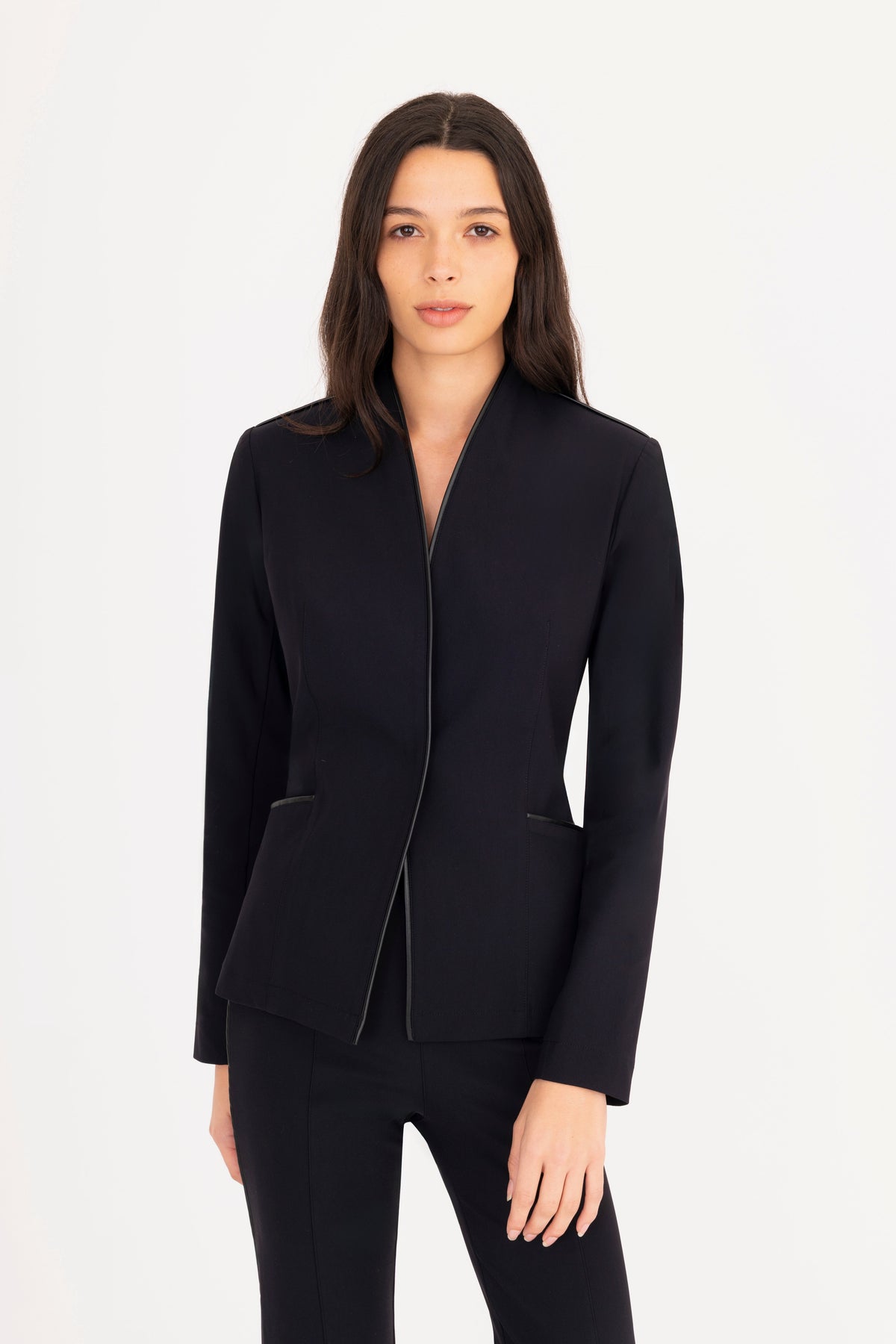 A woman modeling a black structured blazer, paired with black trousers, against a plain white studio background.