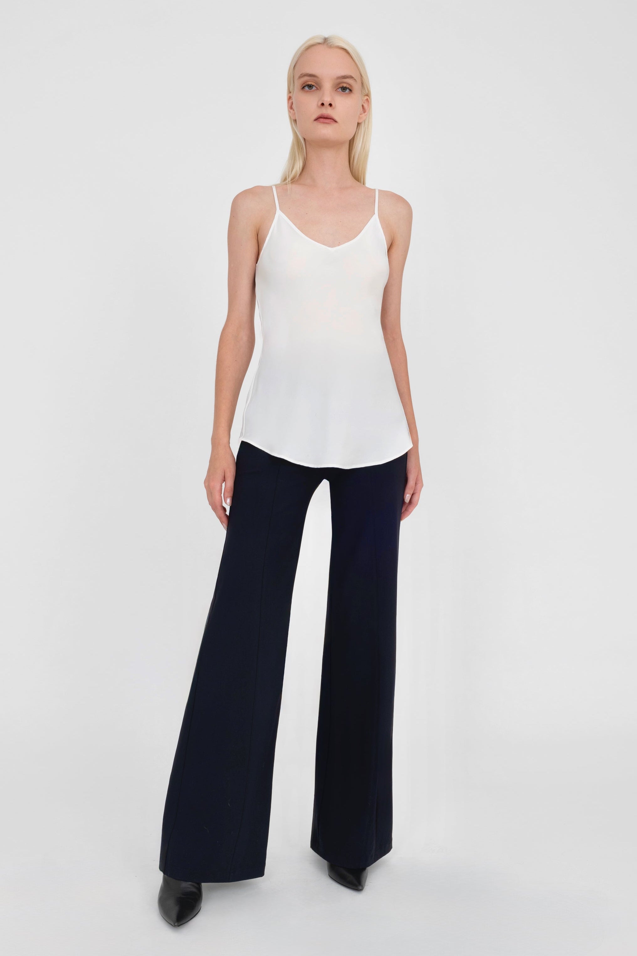 Woman wearing a white sleeveless top and black pants on a white background