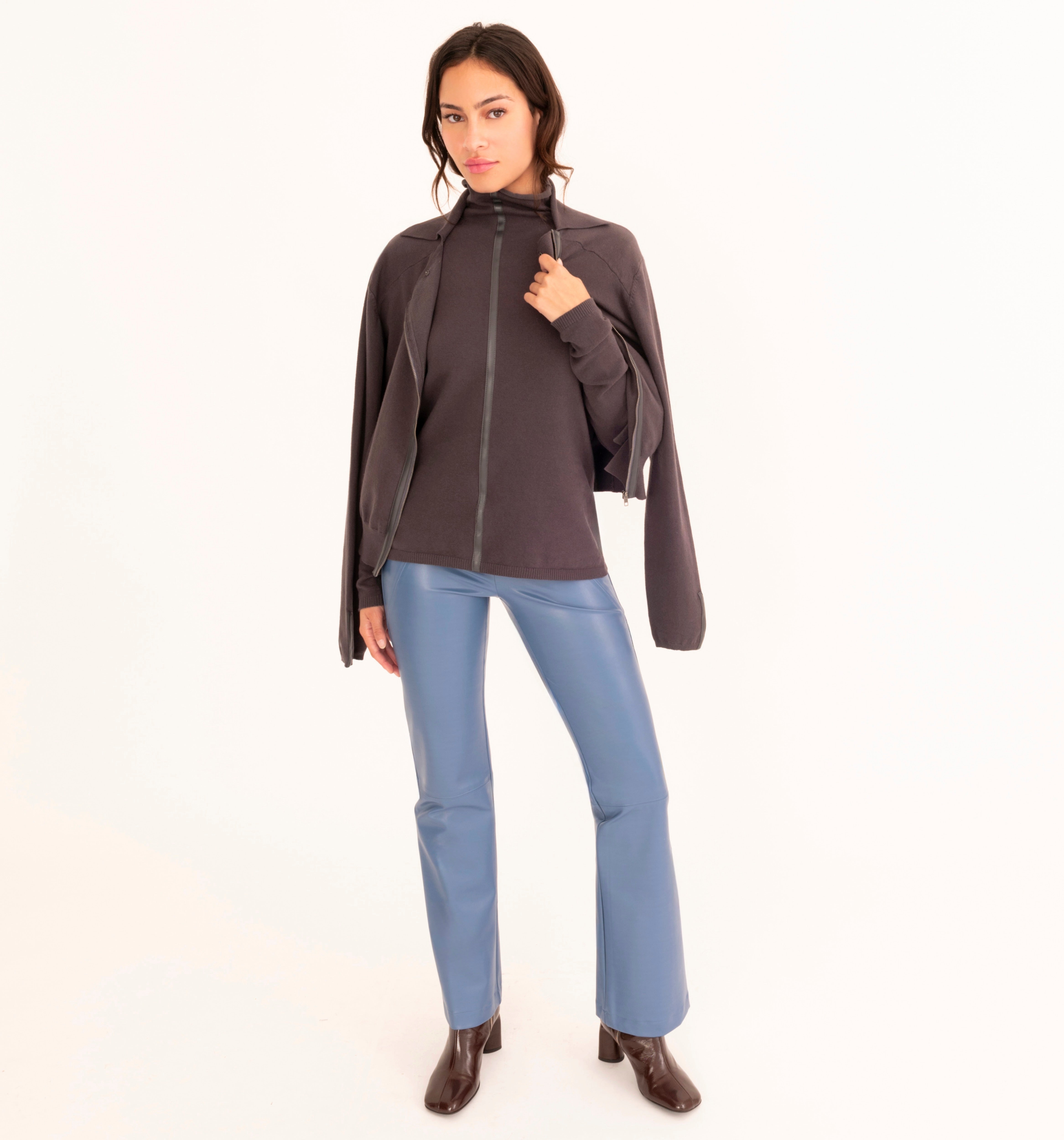 A woman modeling a gray zip-up jacket with wide sleeves, paired with blue pants and dark brown boots, against a plain white studio background.