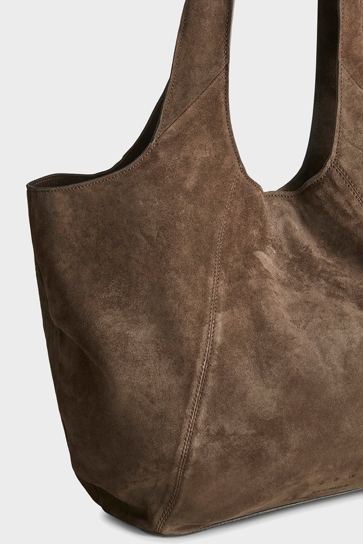 A close-up of a brown suede tote bag with a double shoulder strap, shown against a light gray background.