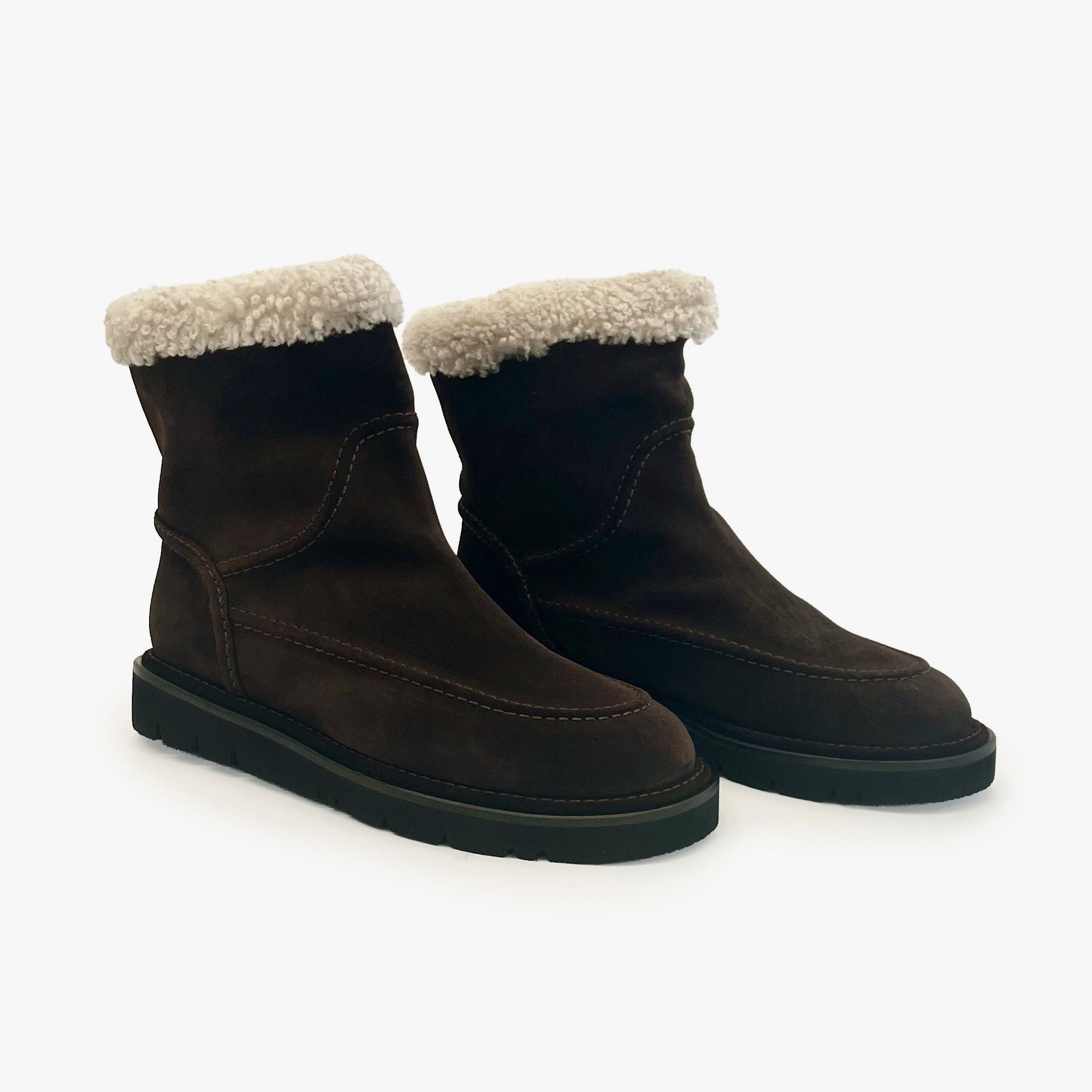 A pair of dark brown suede ankle boots with a thick black sole and a fluffy cream shearling lining at the top, shown on a clean white background.
