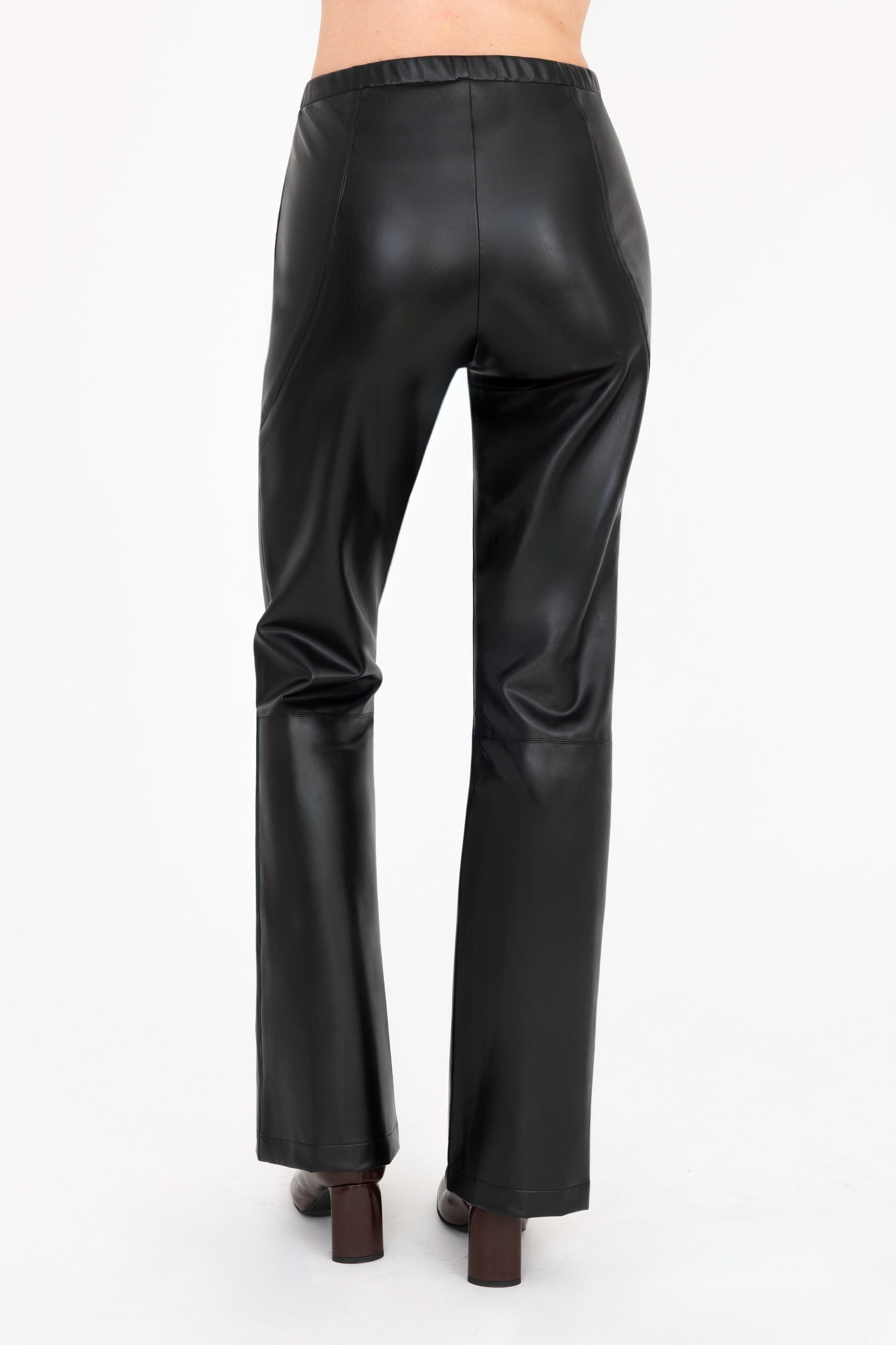 Back view of a model shown from the waist down wearing high-waisted, wide-leg black  faux-leather pants and dark brown heeled boots against a plain off-white background.