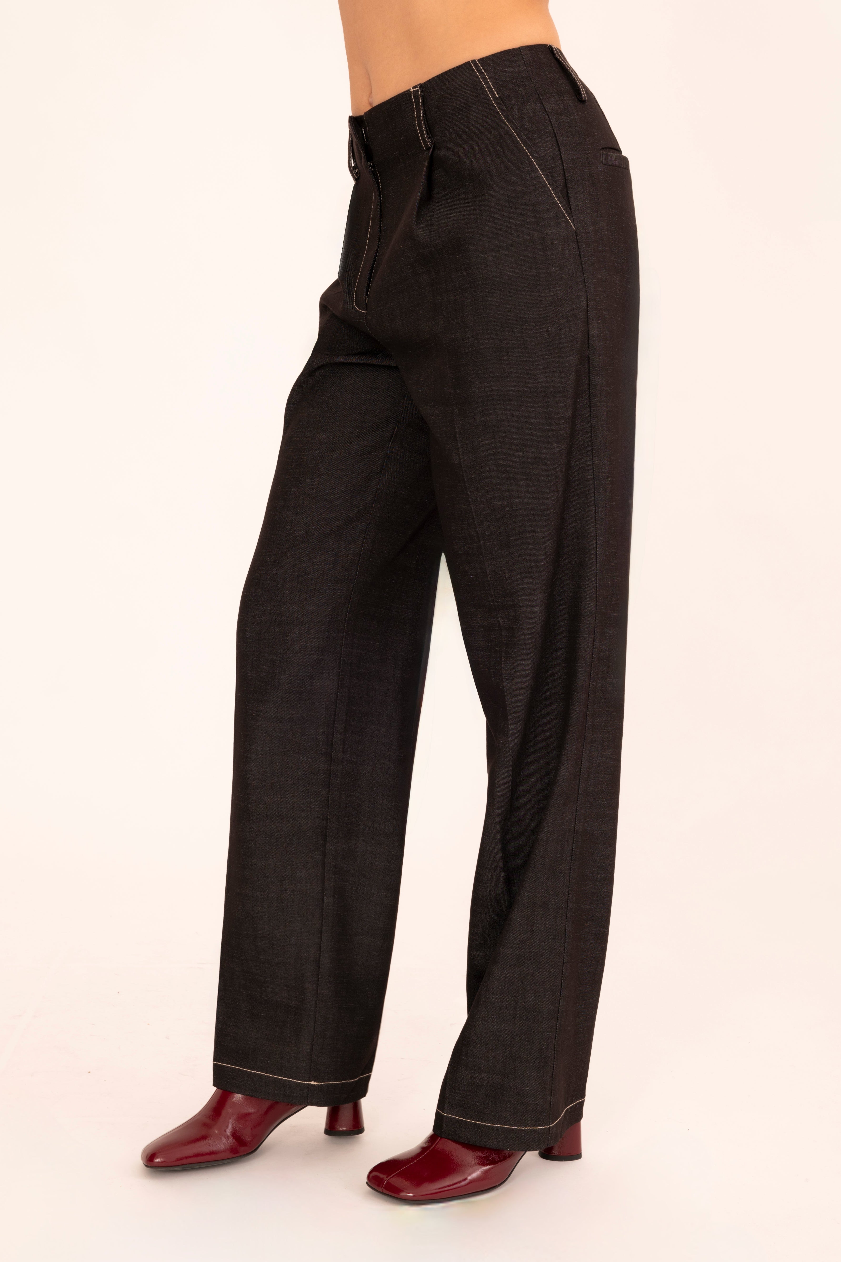 A model is shown from the waist down wearing black denim trousers and dark red shoes, standing against a plain off-white background.