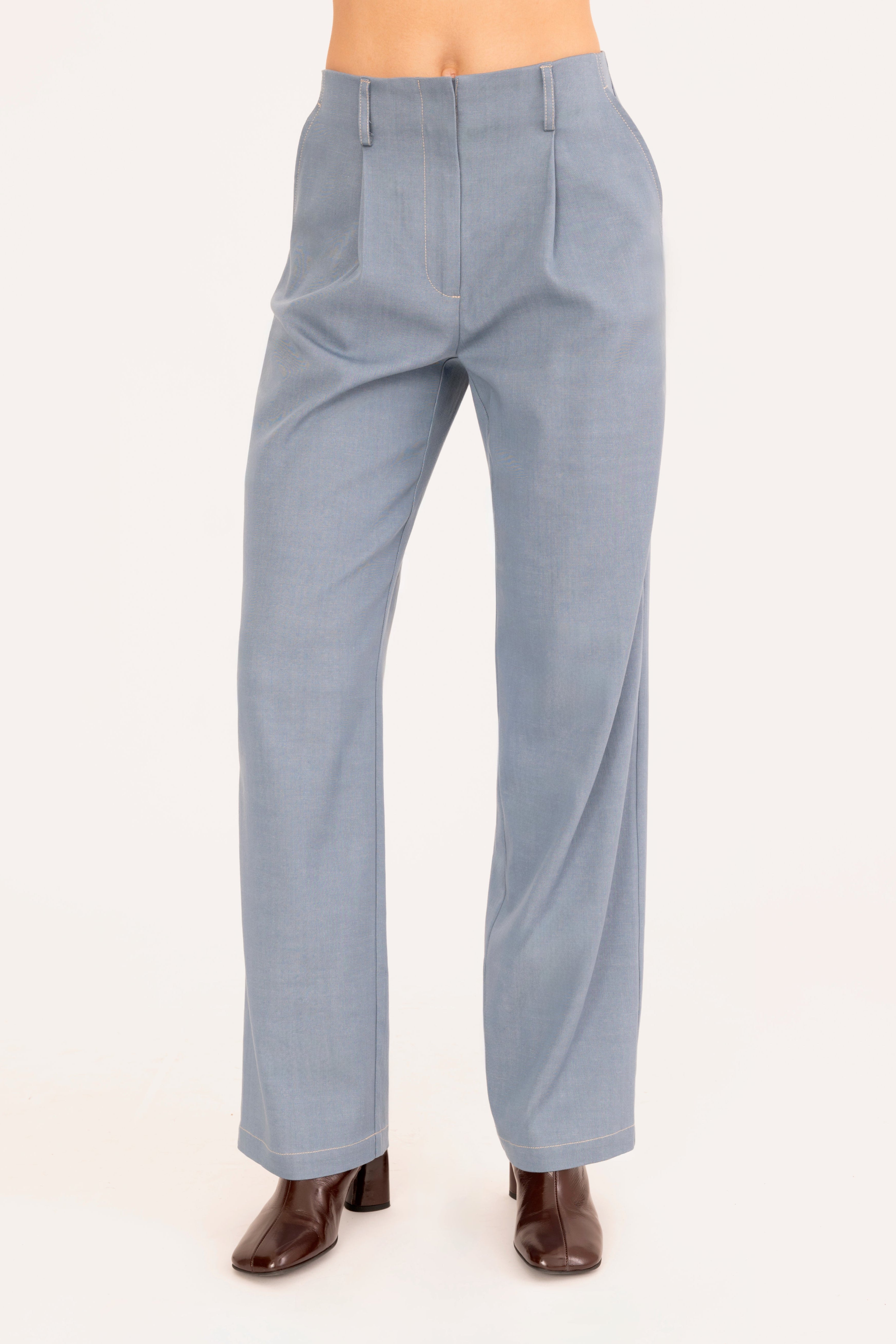 A model is shown from the waist down wearing a pair of light blue denim trousers and dark brown heeled boots against a plain off-white background.