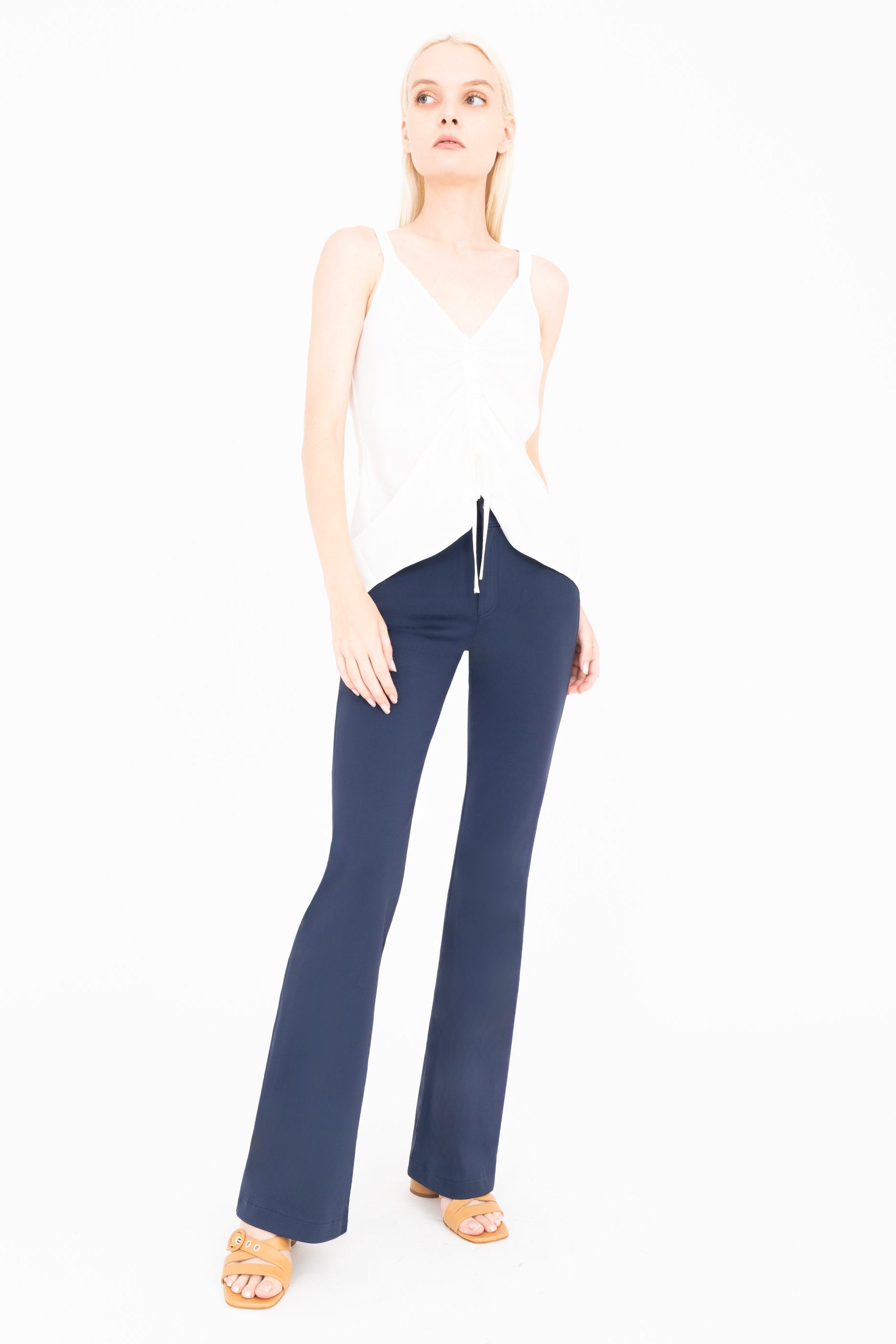 Woman wearing a white sleeveless top and blue flared pants on a white background