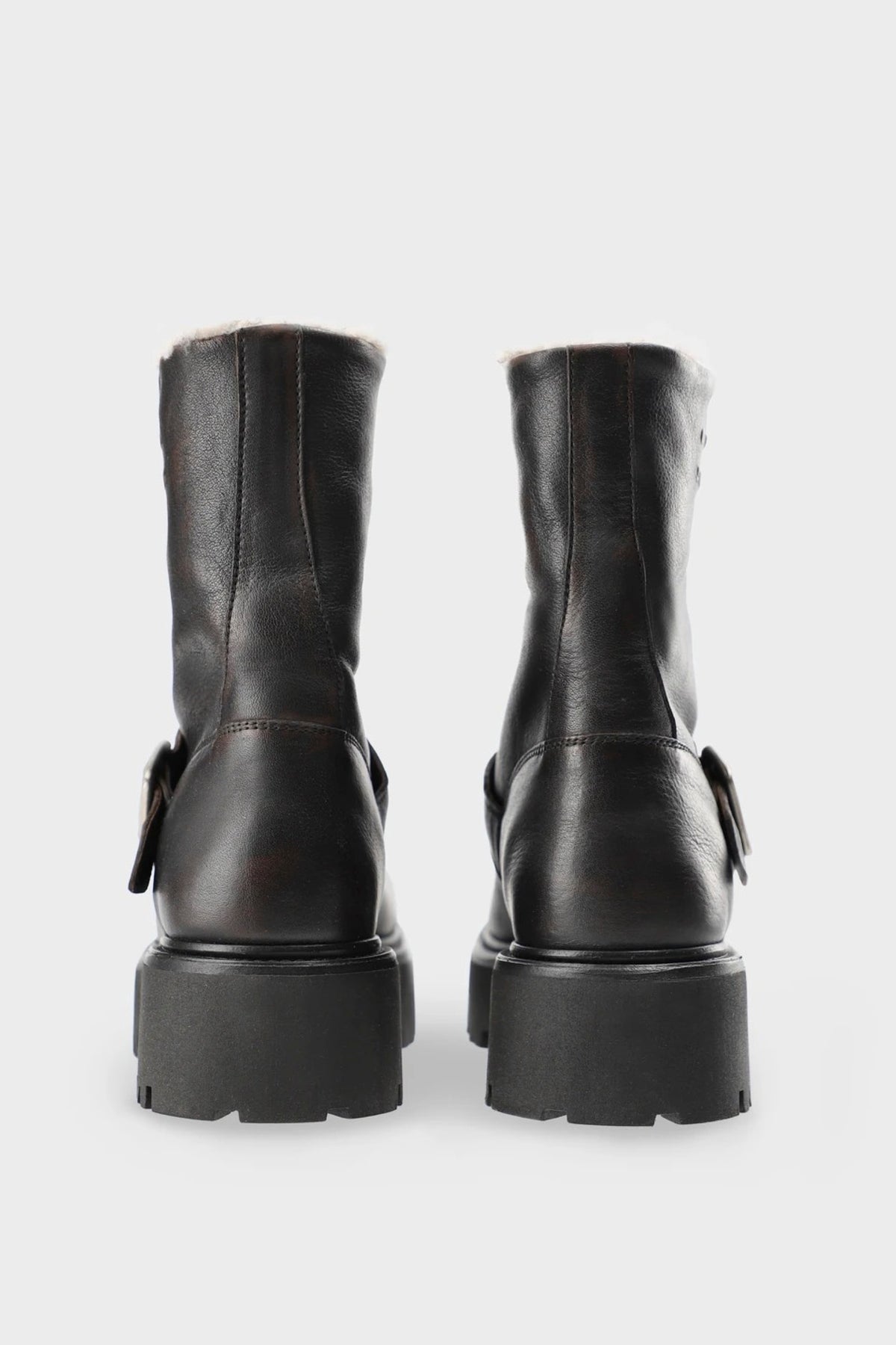 A pair of dark brown leather ankle boots with chunky lug soles and side buckle details, shown from the back against a light gray background.