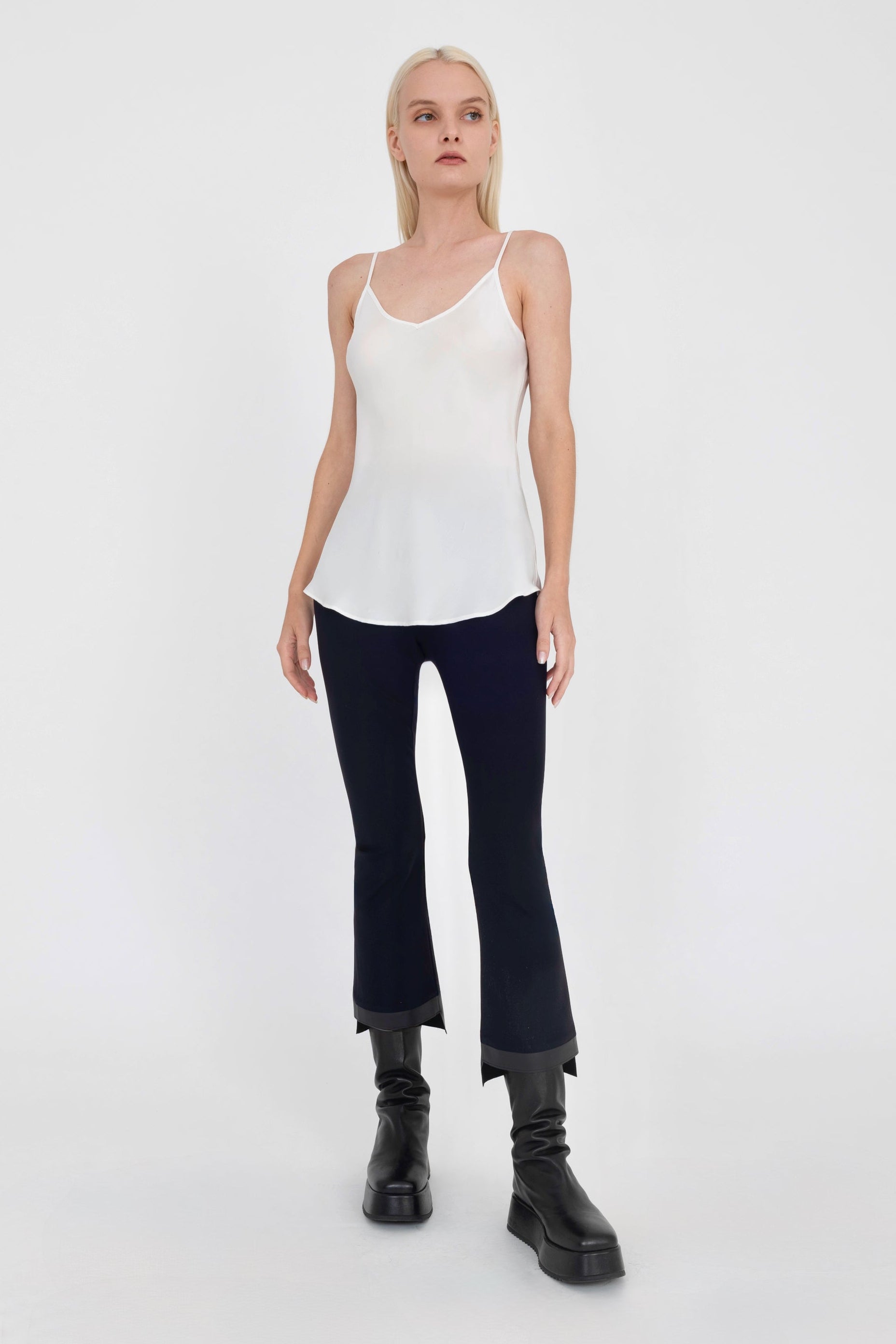 Woman wearing a white tank top and black pants on a white background