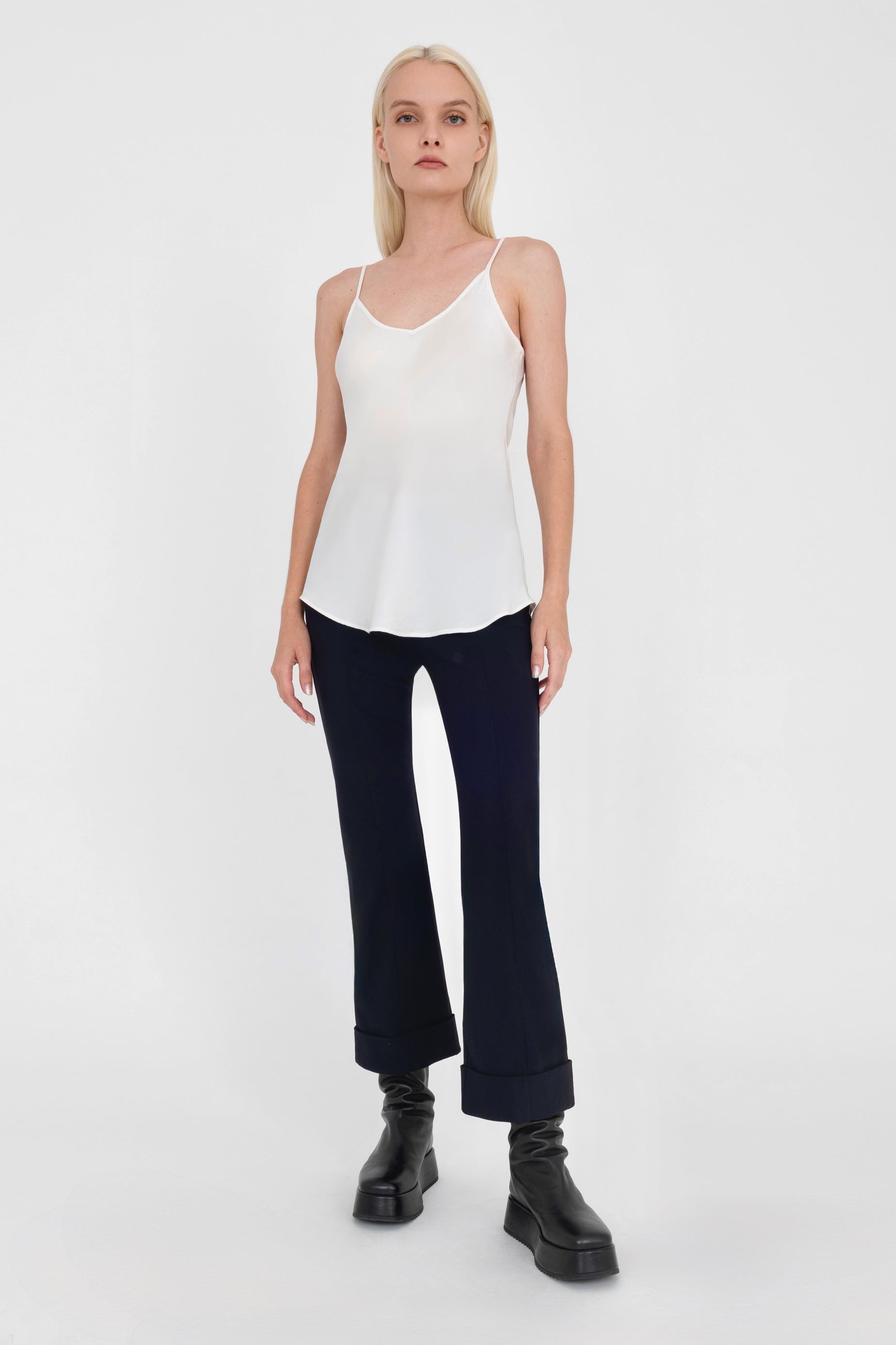 Woman wearing a white sleeveless top and black pants on a white background