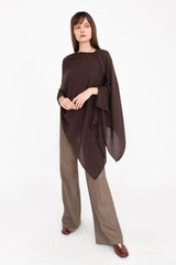 Woman wearing a brown poncho over a dark top and light pants on a white background
