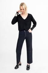 Woman wearing a black long-sleeve top and dark jeans on a white background